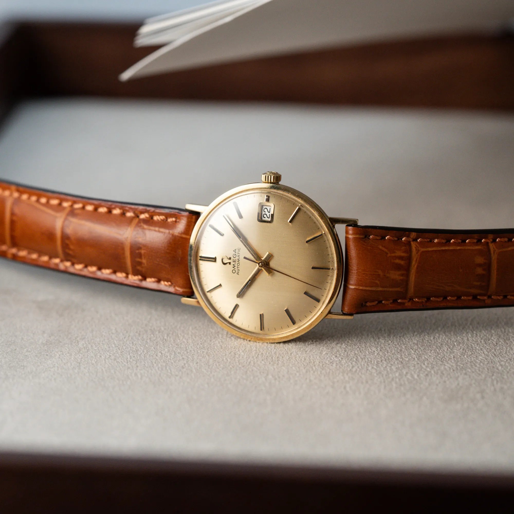Produktfotografie der seitlich liegenden Omega Vintage Automatik Armbanduhr mit Gelbgold-Gehäuse
