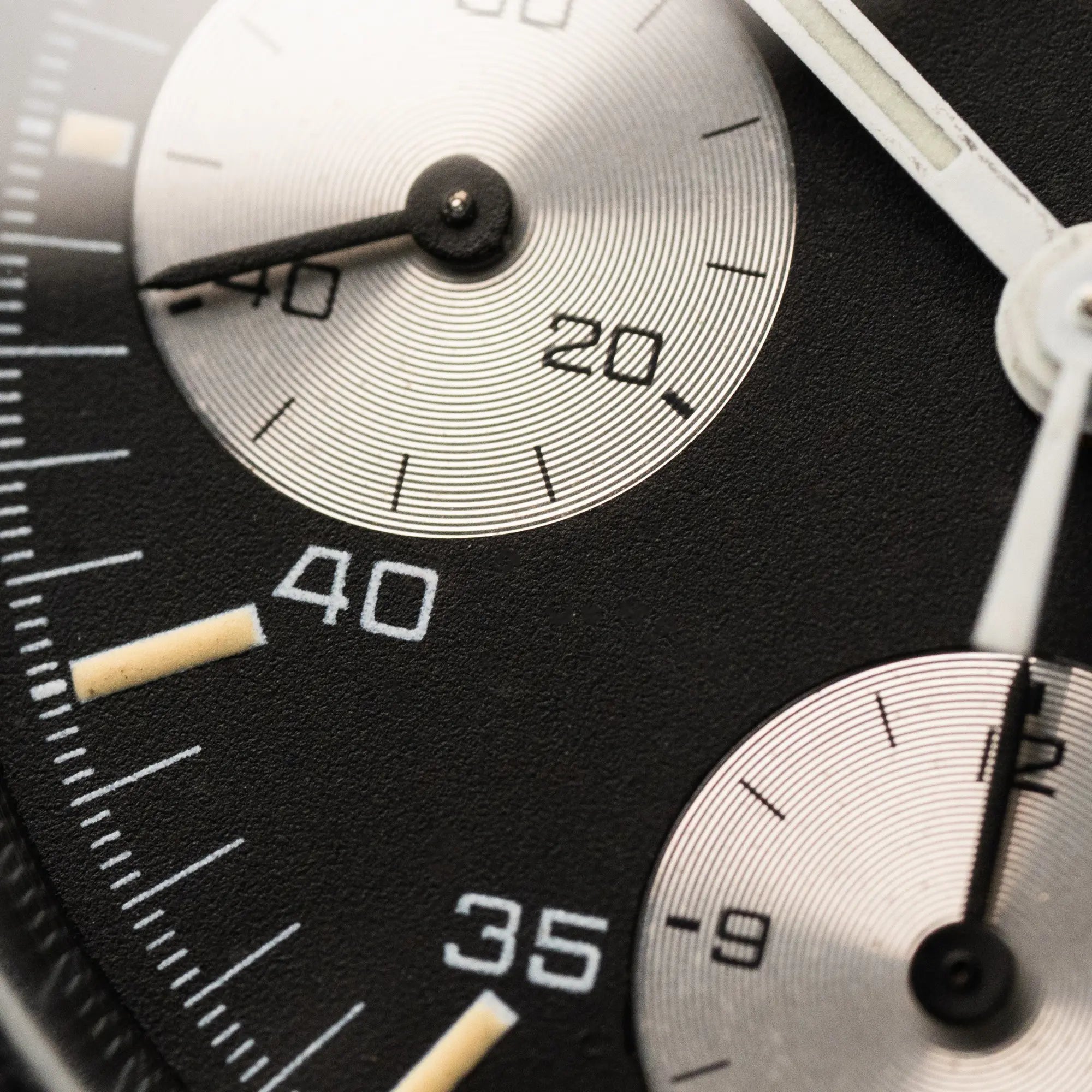 Makroaufnahme des Zifferblatts der Omega Speedmaster Automatic Date mit schwarzem Zifferblatt und silbernen Totalisatoren und gleichmäßig leicht vergilbten Indizes