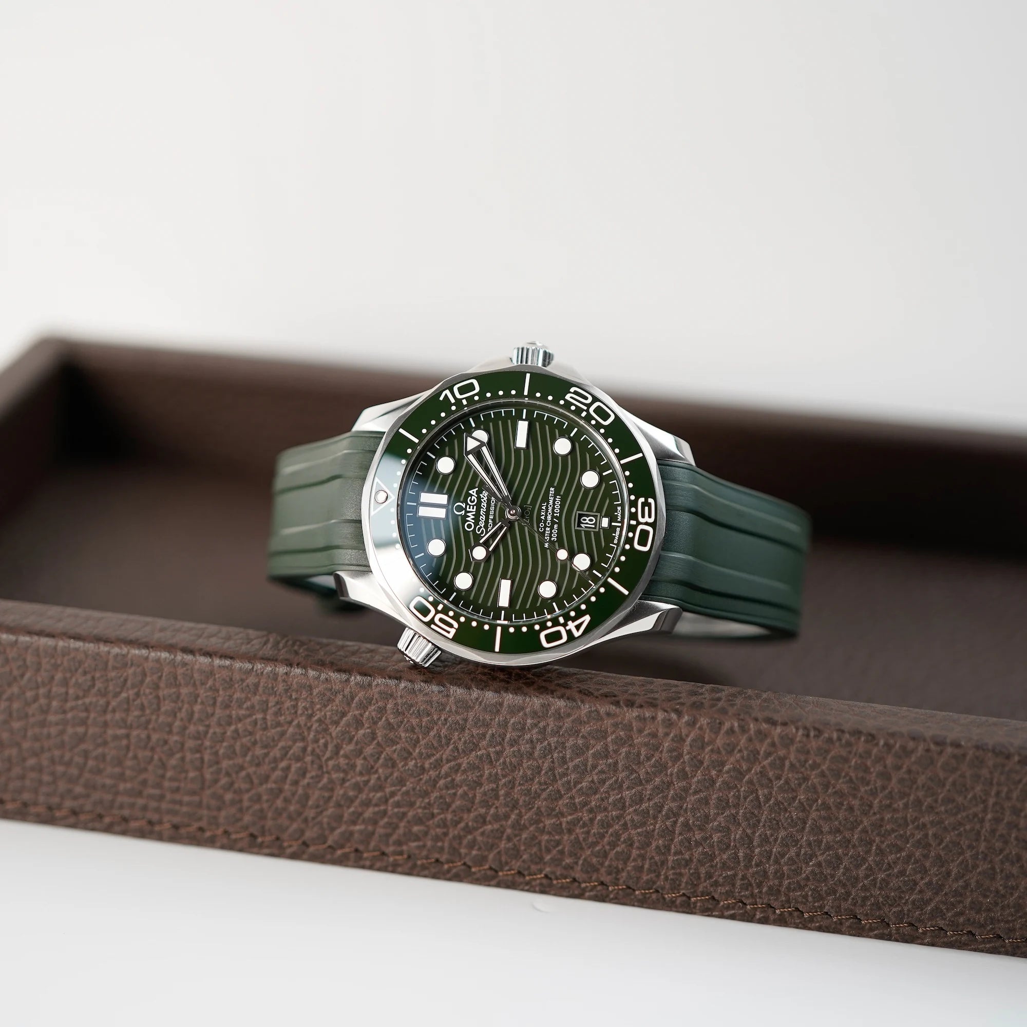 Liegende Omega Seamaster Professional Diver 300m an einem olivgrünen Kautschukband liegt auf braunem Leder Tablet