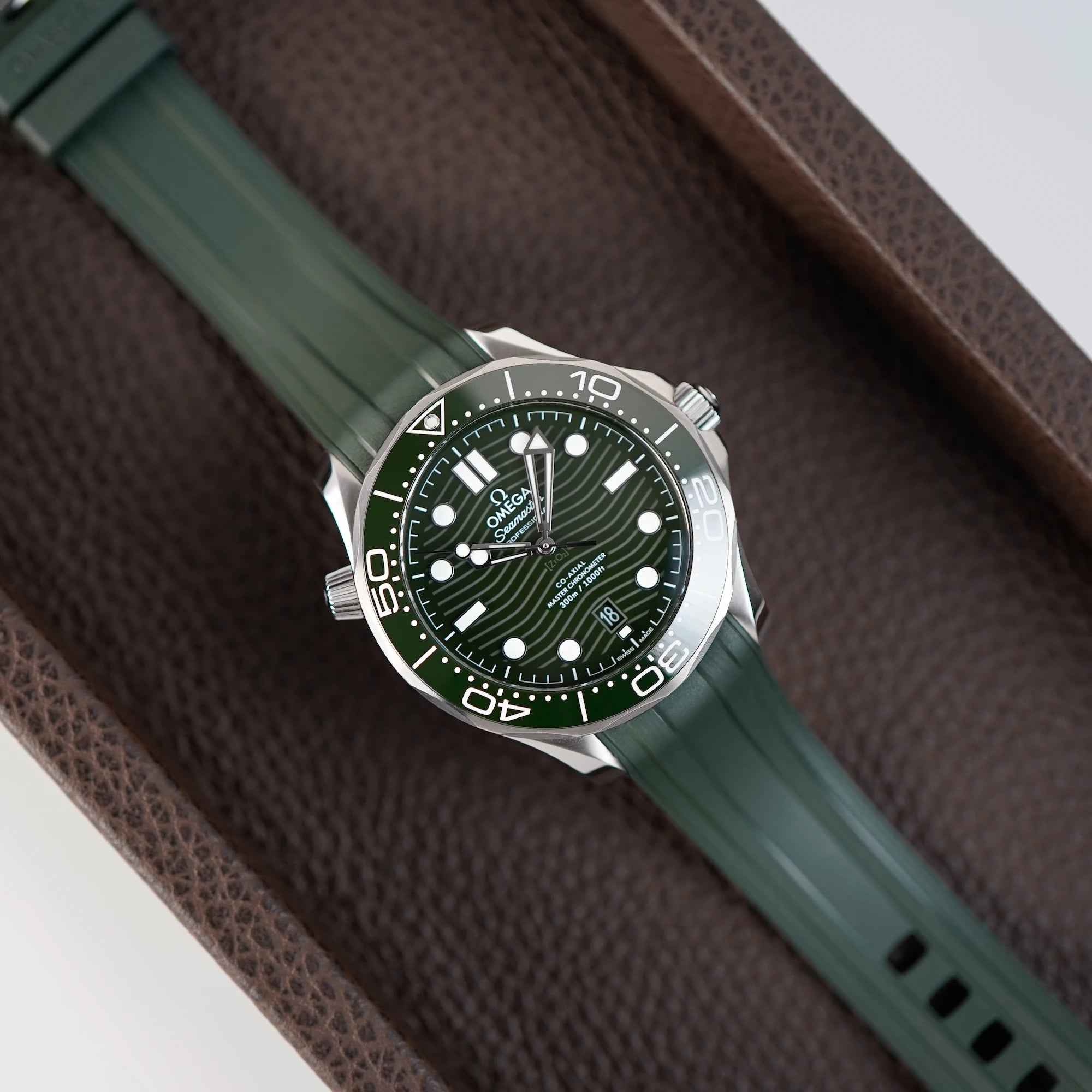 Omega Seamaster Professional Diver 300m an einem olivgrünen Kautschukband liegt auf braunem Leder Tablet