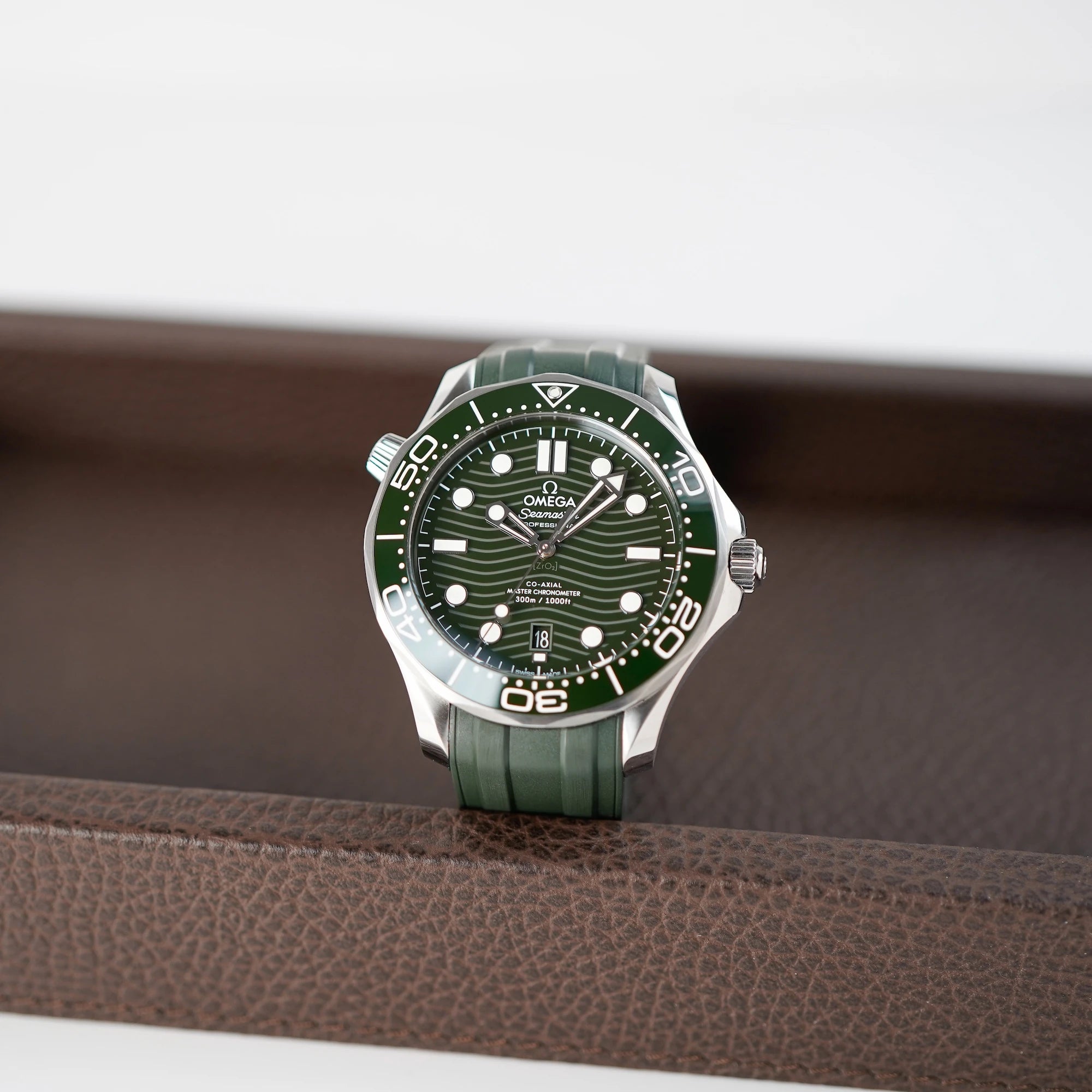 Frontaler Blick auf die Liegende Omega Seamaster Professional Diver 300m an einem olivgrünen Kautschukband auf braunem Leder Tablet
