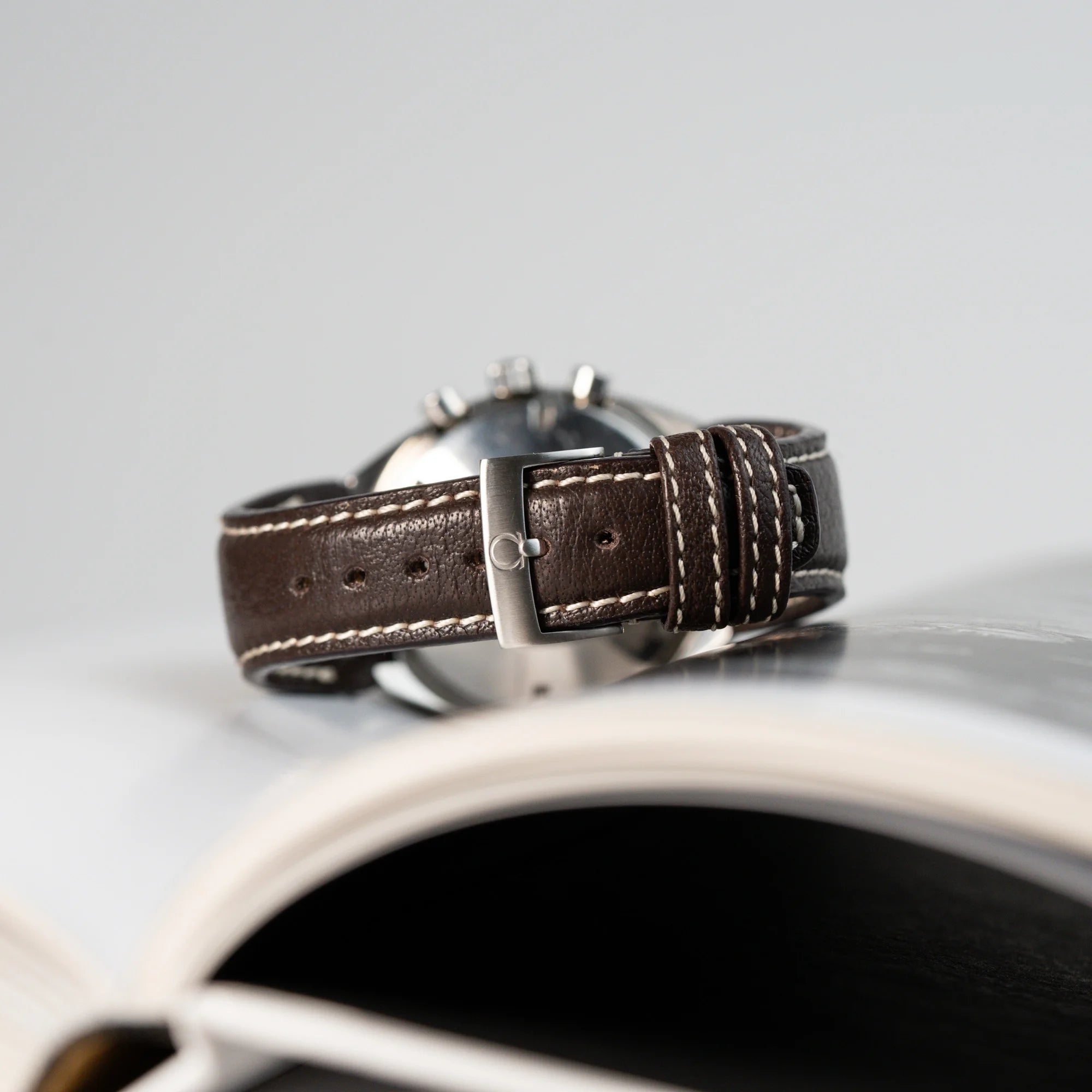 Produktfotografie des braunen Rios-Lederbands mit originaler Omega-Dornschliesse der Produktfotografie der liegenden Omega Speedmaster Moonwatch Mark 2