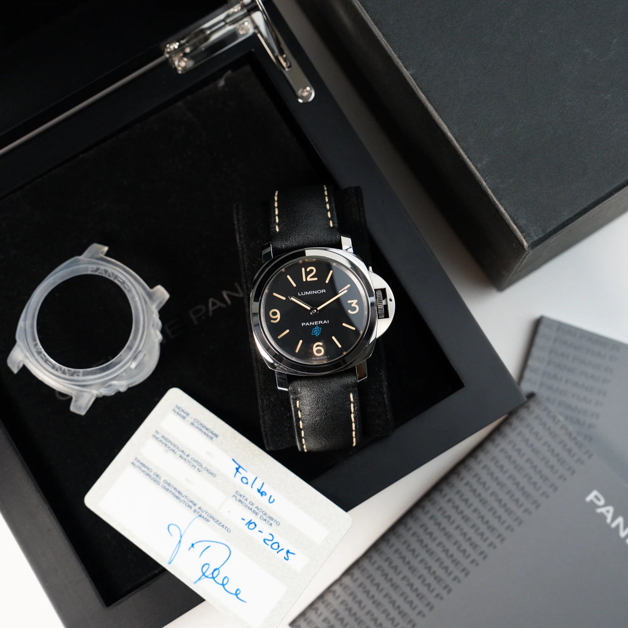 Lieferumfang der Panerai Luminor Logo Base mit schwarzem Zifferblatt und beigen Indizes, sowie einen schwarzem Lederband, betsehend aus Box, Booklets, Garantiekarte und Lünetten-Schutz