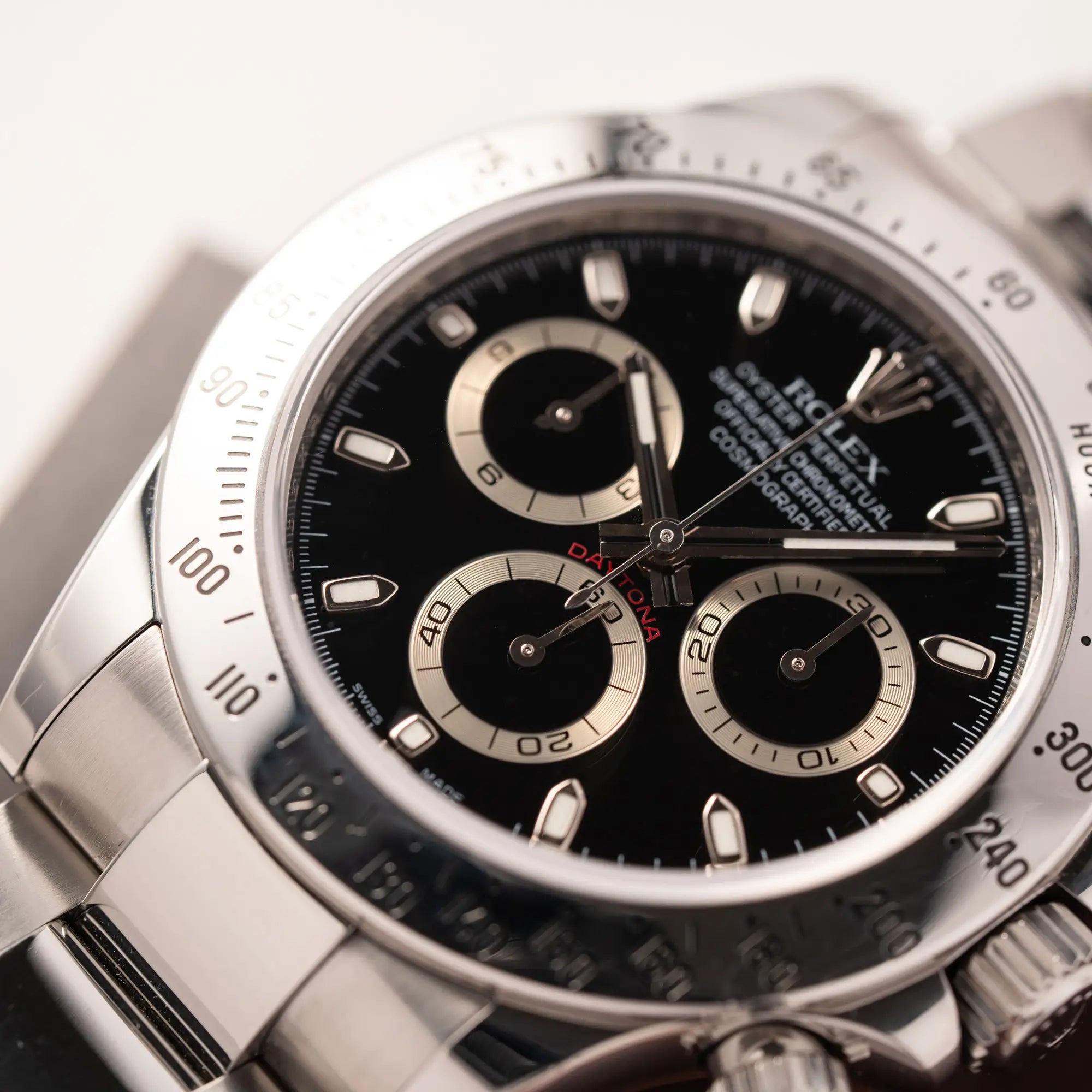 Detailaufnahme mit Fokus auf dem Zeigersatz der Rolex Cosmograph Daytona 116520 mit schwarzem Zifferblatt und der klassischen Edelstahl-Lünette vor Umstellung auf die Keramik-Lünette