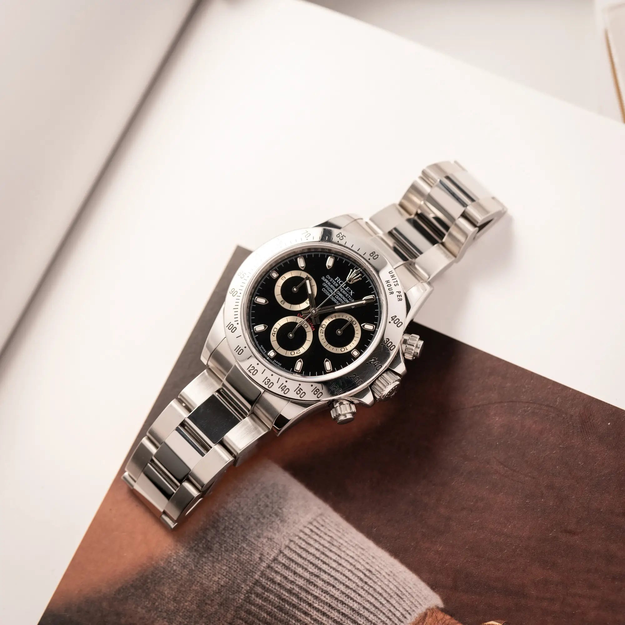 Rolex Cosmograph Daytona 116520 mit schwarzem Zifferblatt und der klassischen Edelstahl-Lünette vor Umstellung auf die Keramik-Lünette liegt flach auf einem Uhrenbuch