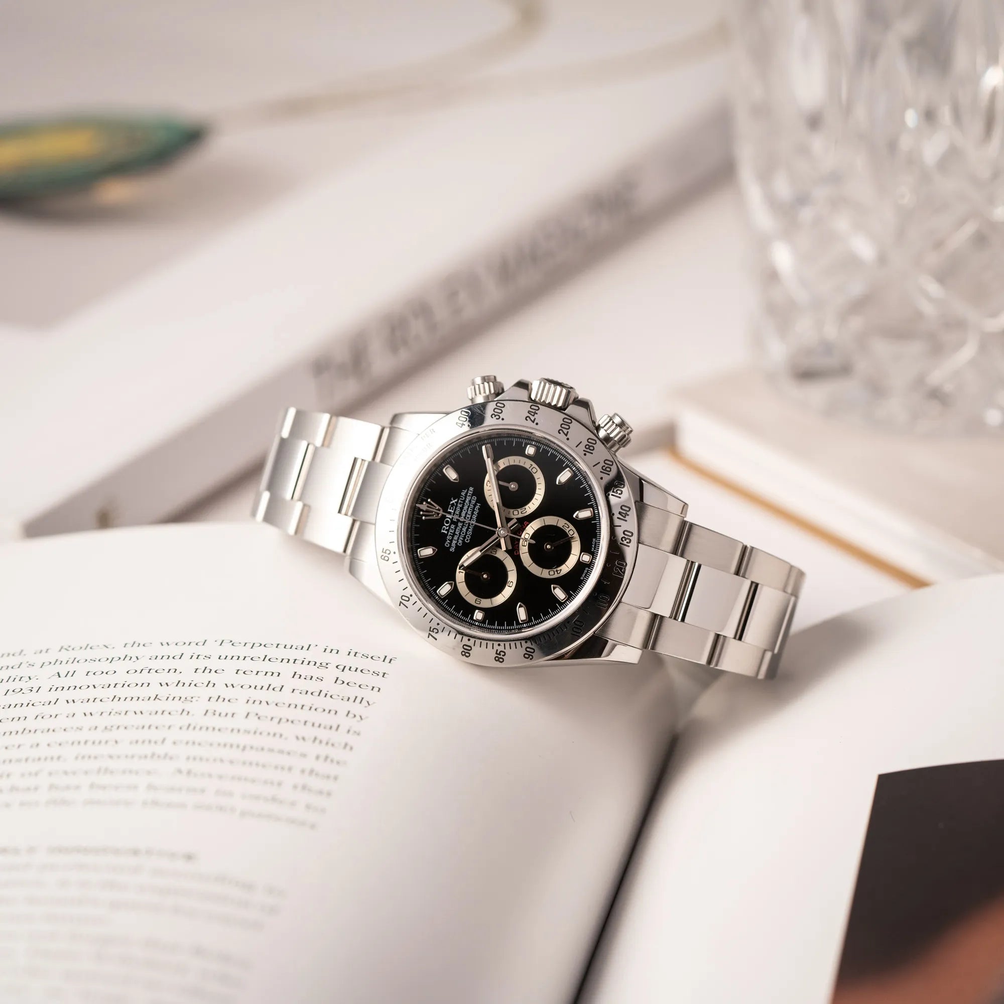 Produktoftografie der seitlich auf dem Uhrengehäuse liegenden Rolex Cosmograph Daytona 116520 mit schwarzem Zifferblatt und der klassischen Edelstahl-Lünette vor Umstellung auf die Keramik-Lünette