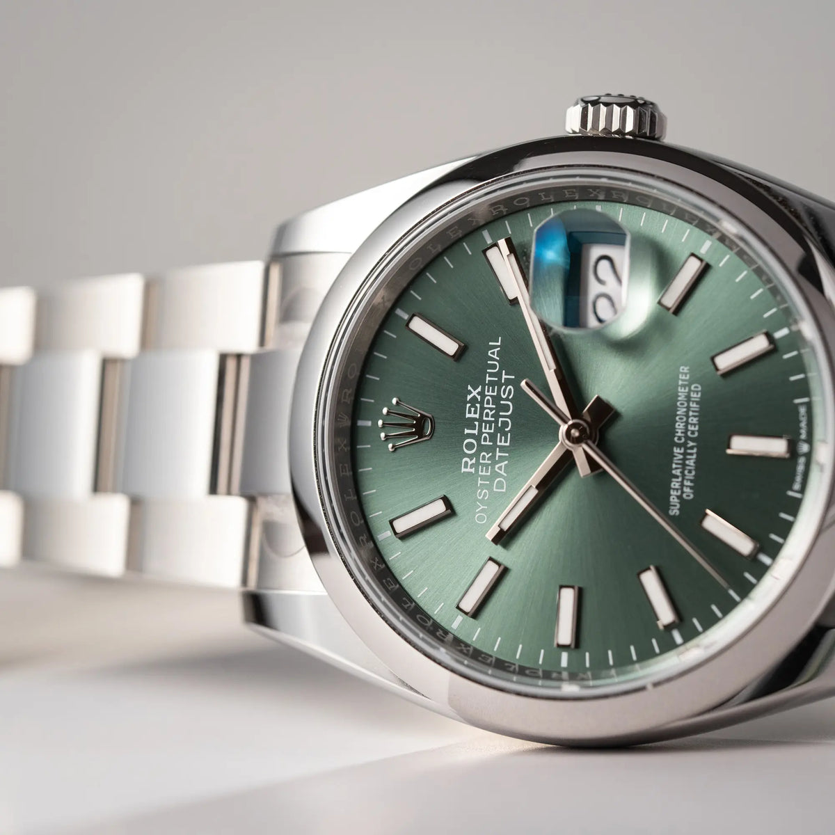 Detailaufnahme der seitlich auf dem Uhrengehäuse liegende, mit Stickern teil-verklebte Rolex Datejust 36 der Referenz 126200 mit glatter Lünette am Oyster-Stahlband mit dem Mint-Green-Zifferblatt