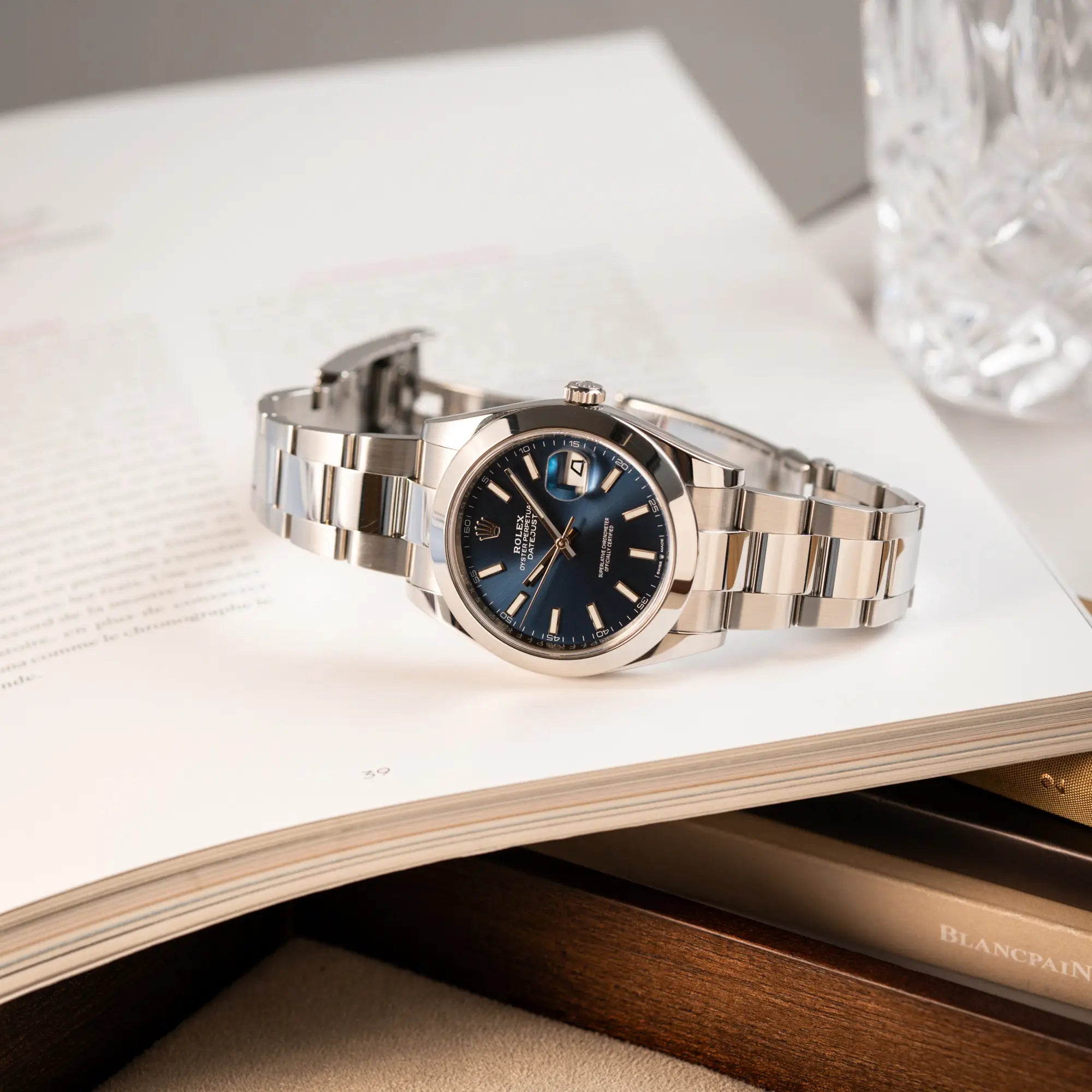 Produktfotografie der Rolex Datejust 41 der Referenz 126300 mit blauem Zifferblatt, glatter Lünette, am Oyster-Stahlband, während die Uhr auf einem Buch liegt