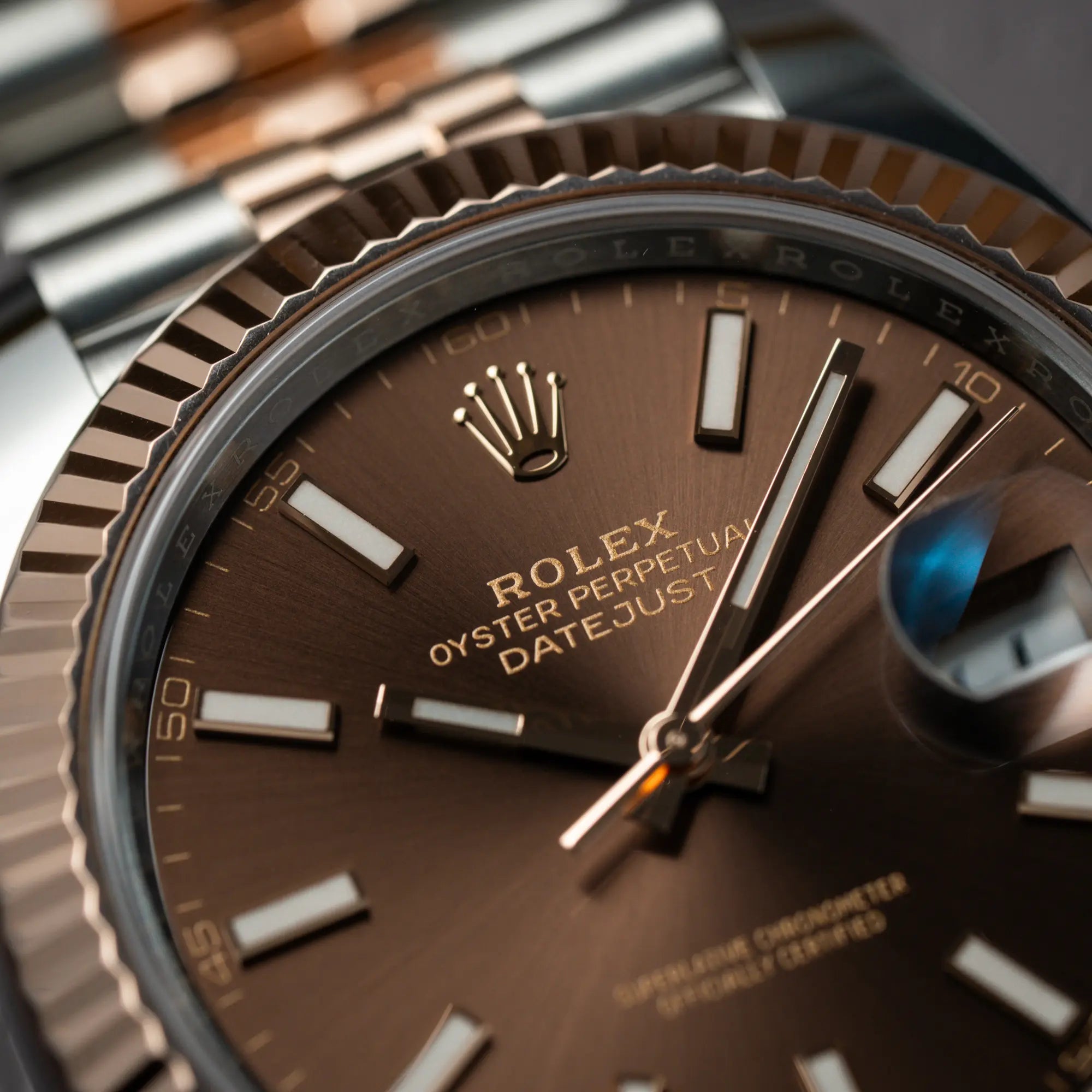 Makroaufnahme der bicolor Rolex Datejust 41 der Referenz 126331 Chocolate in Stahl-Roségold mit einem zum Roségold passenden braunen Zifferblatt am zugehörigen Jubilee-Armband mit Fokus auf dem "Rolex Oyster Perpetual Datejust" -Schriftzug bei 12 Uhr