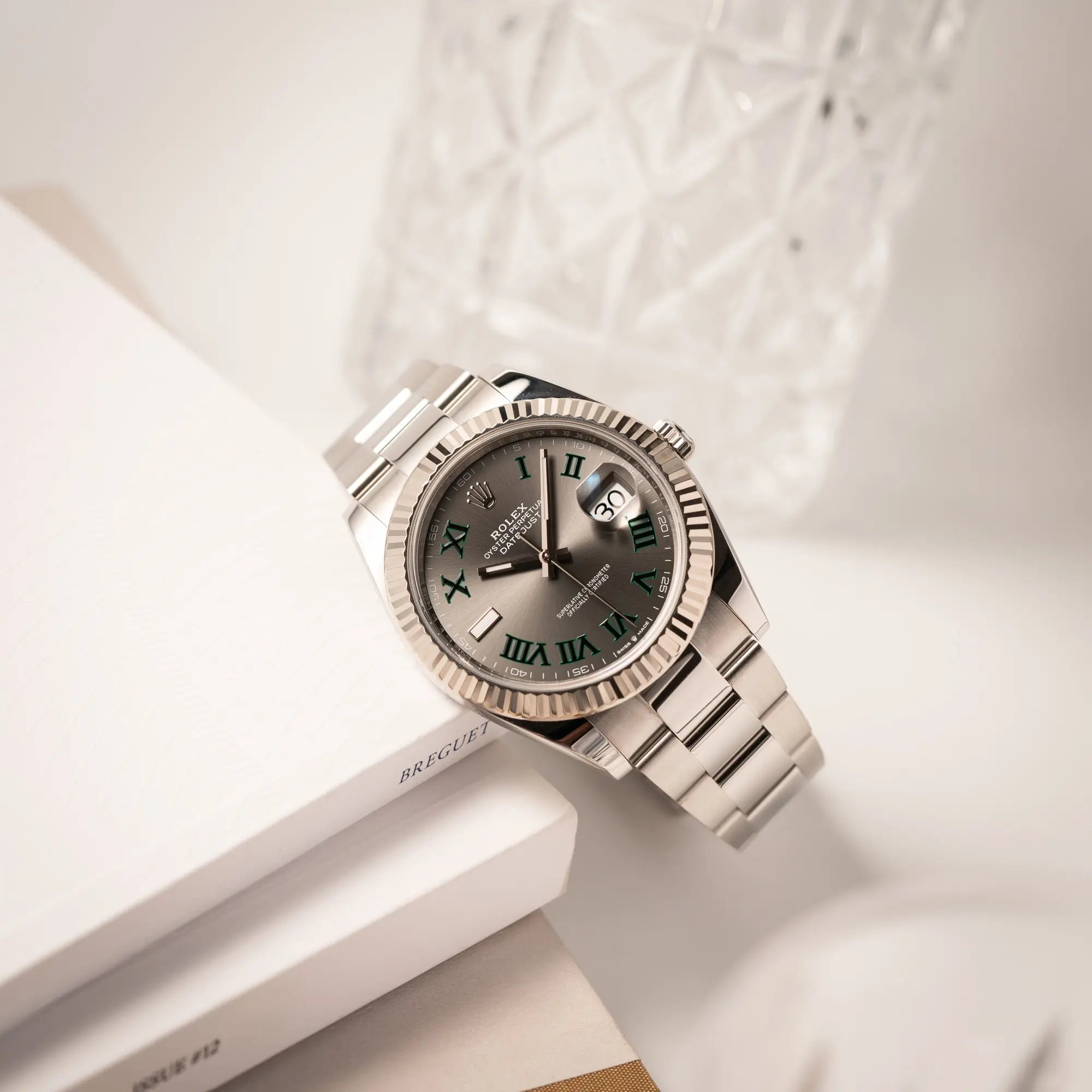 Produktfotografie als Titelbild für die Rolex Datejust 41 der Referenz 126334 mit geriffelter Weißgold-Lünette und Oyster-Stahlband mit dem grauen Wimbledon-Zifferblatt mit schwarz-grünen Indizes