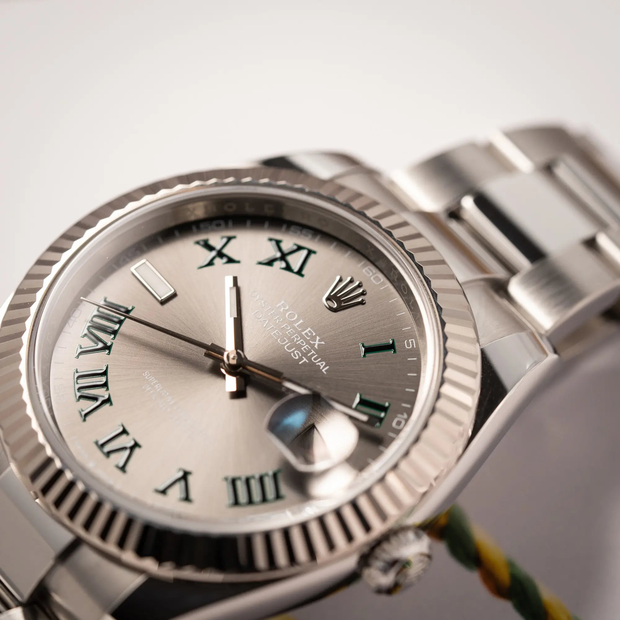 Detailaufnahme des Sonnenschlif-Dials der Rolex Datejust 41 der Referenz 126334 mit geriffelter Weißgold-Lünette und Oyster-Stahlband mit dem grauen Wimbledon-Zifferblatt mit schwarz-grünen Indizes