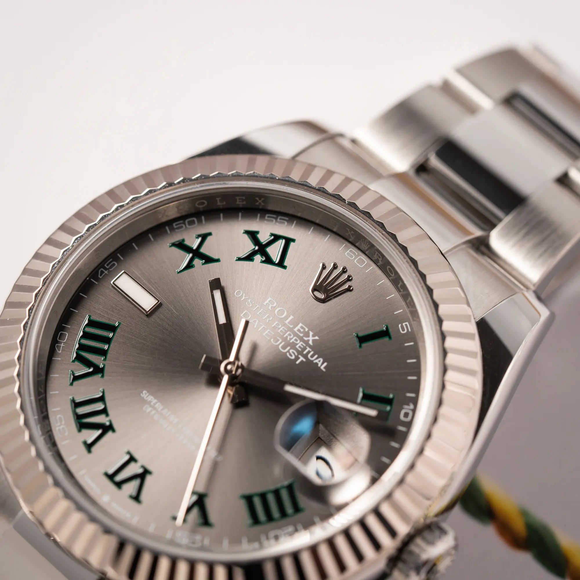 Detailaufnahme der Rolex Datejust 41 der Referenz 126334 mit geriffelter Weißgold-Lünette und Oyster-Stahlband mit dem grauen Wimbledon-Zifferblatt mit schwarz-grünen Indizes