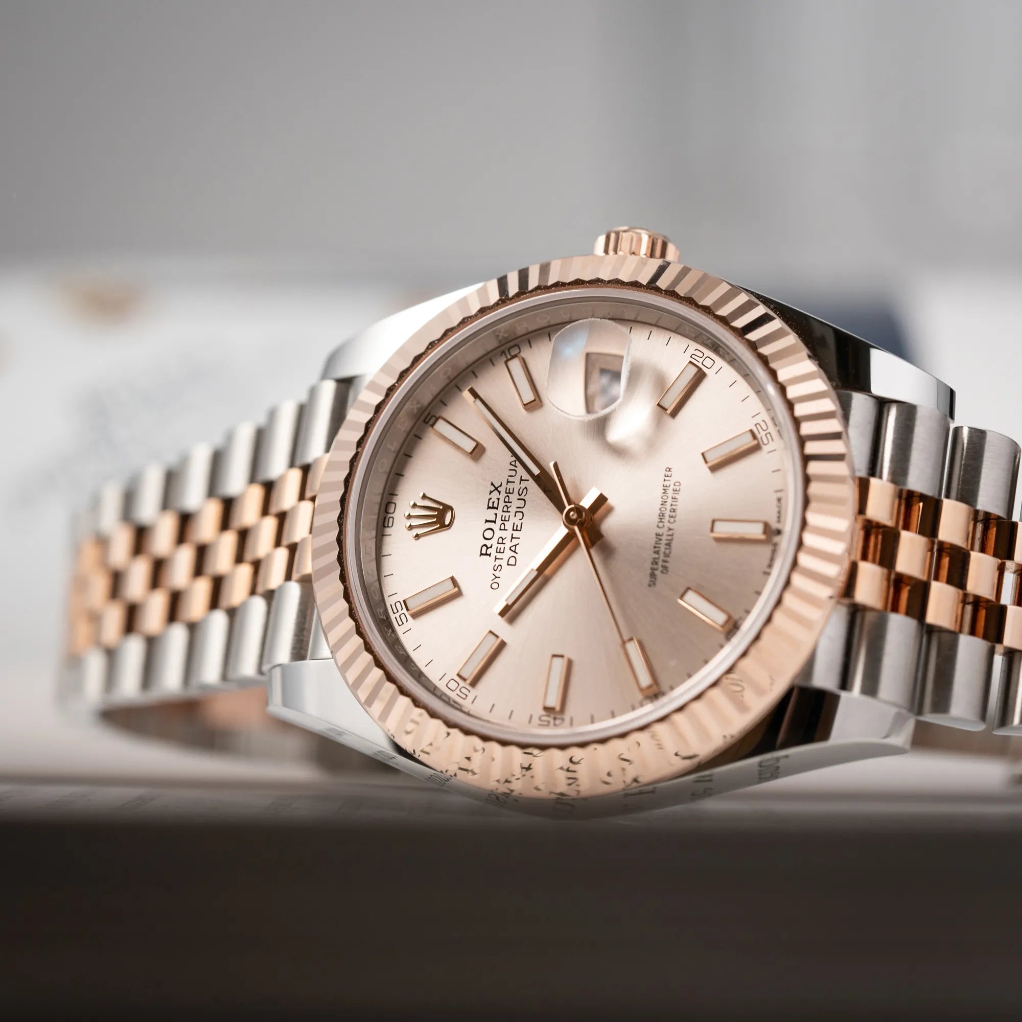 Produktfotografie mit Fokus auf dem Farbverlauf des sonnengeschliffenen Zifferblatts der Rolex Datejust 41 in Stahl-Roségold mit am passenden Jubilee-Armband mit dem pink-lachsfarbenen "Sundust" Zifferblatt