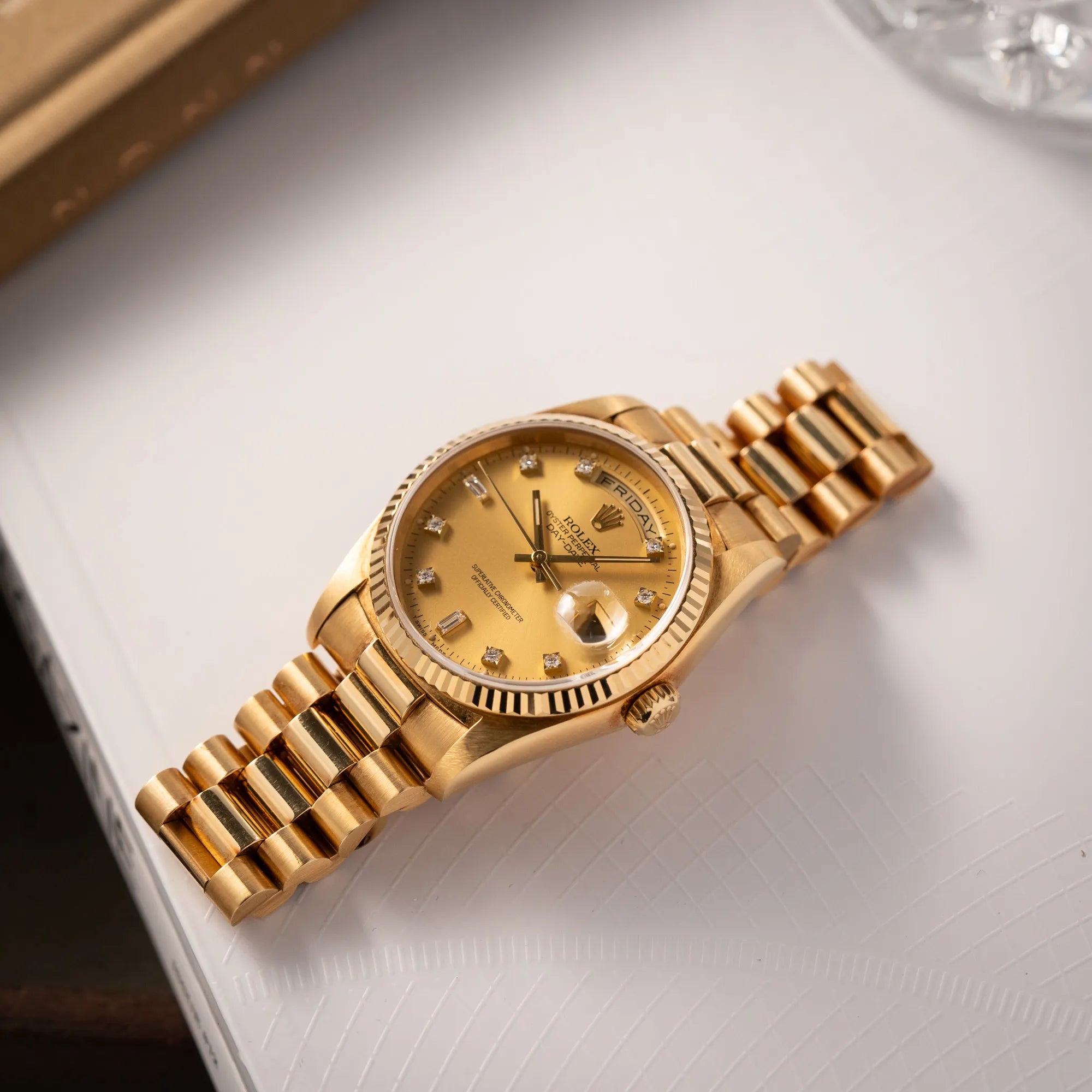 Produktfotografie der flach auf einem Buch liegenden Rolex Day-Date 36 der Referenz 18238 mit champagnerfarbenem Diamant-Zifferblatt