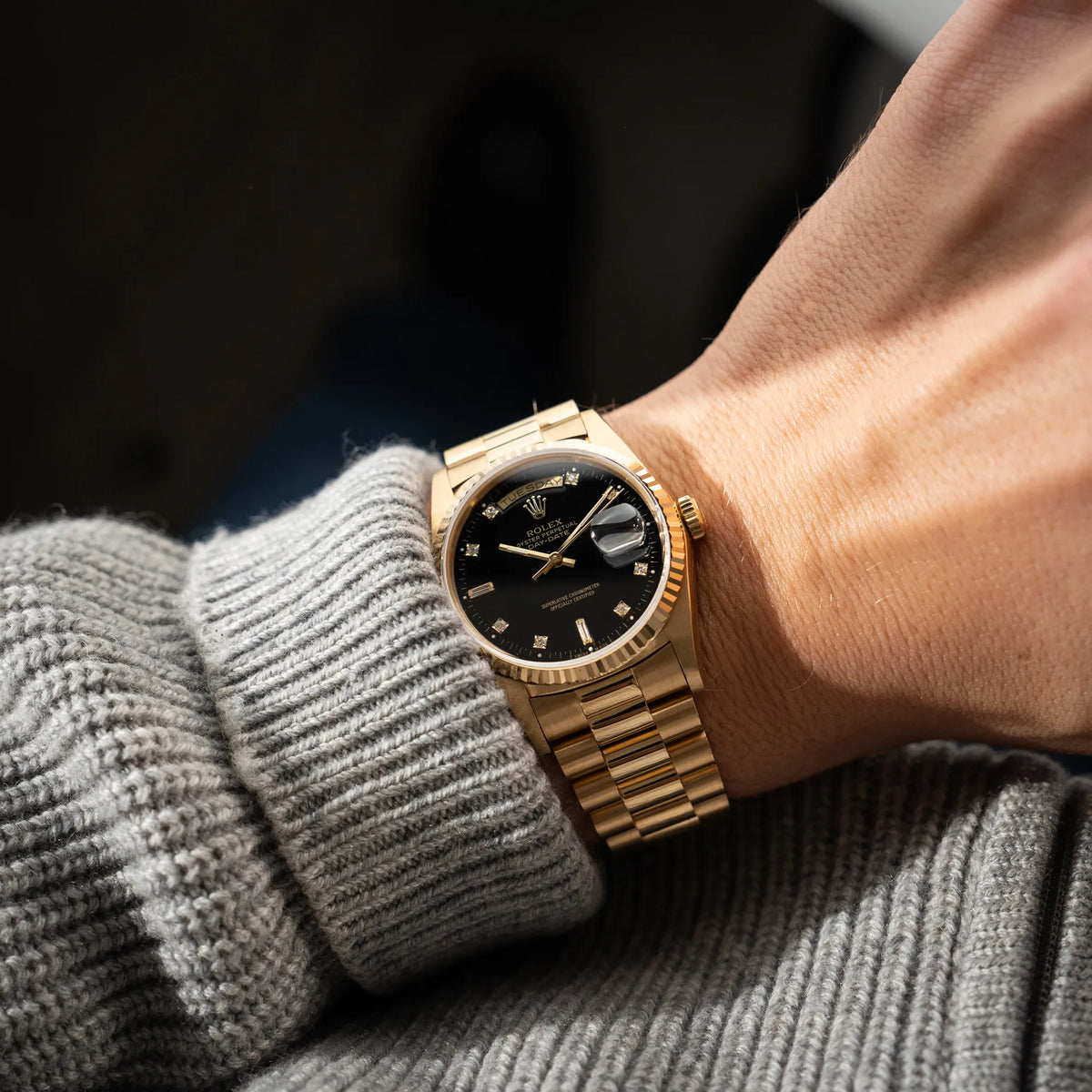 Mann in grauem Pullover trägt die Rolex Day-Date 36 der Referenz 18238 in Gelbgold mit schwarzen Diamond-Dial am President-Armband an seinem Handgelenk