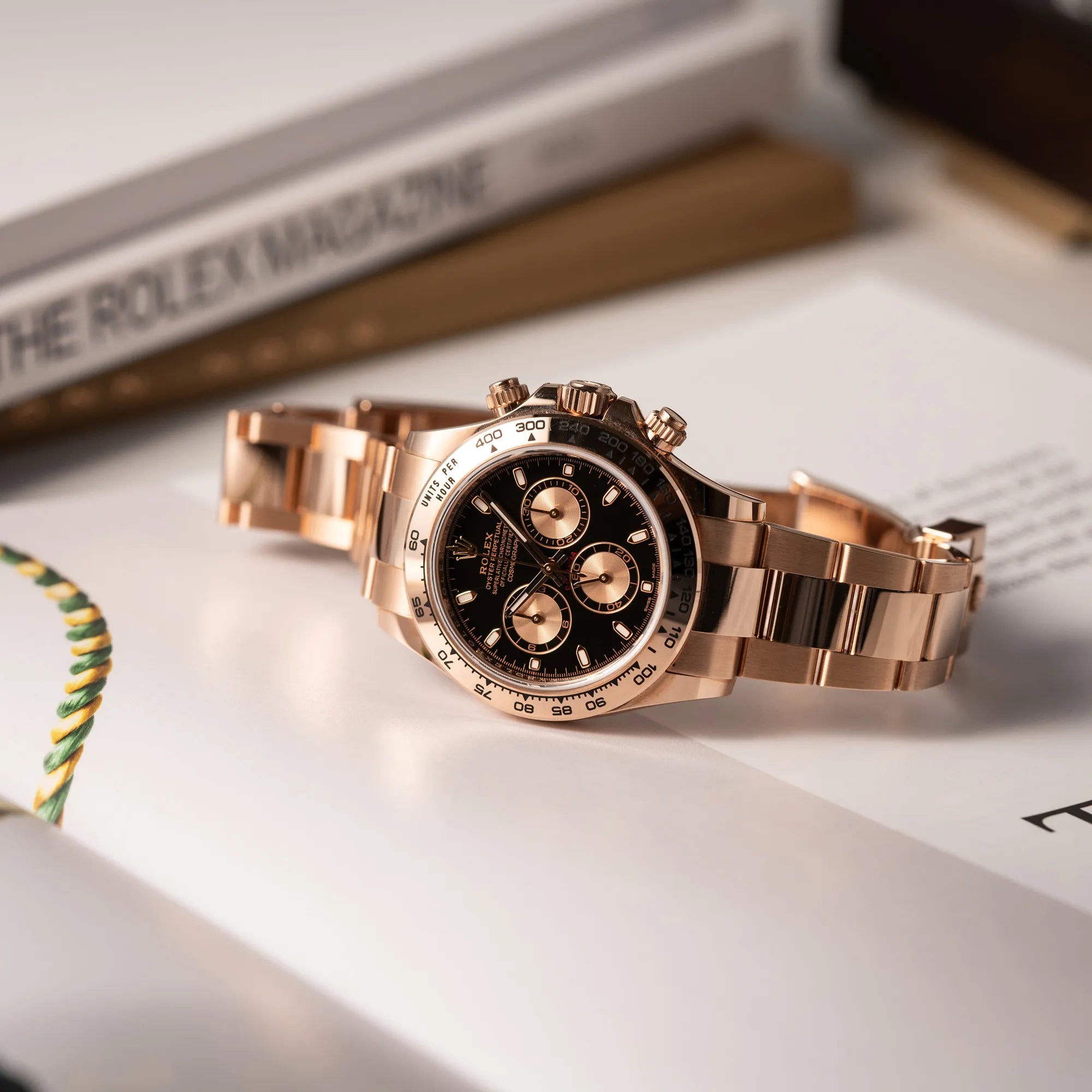 Produktfoto der Rolex Daytona Chronograph-Armbanduhr der Referenz 116505 in Everrose-Roségold mit schwarzem Zifferblatt am Oyster-Roségold-Band, während die Uhr auf einem Uhren-Buch leigt