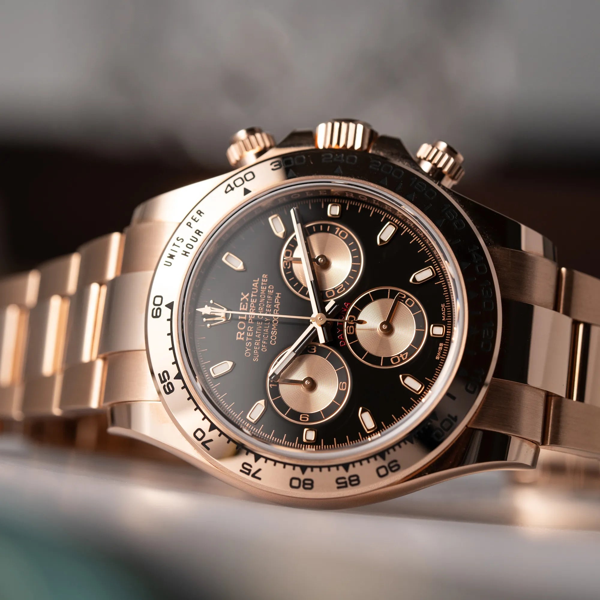 Produktfotografie zeigt die Rolex Daytona Chronograph-Armbanduhr der Referenz 116505 in Everrose-Roségold mit schwarzem Zifferblatt am Oyster-Roségold-Band, während die Uhr seitlich auf dem Gehäuse liegt