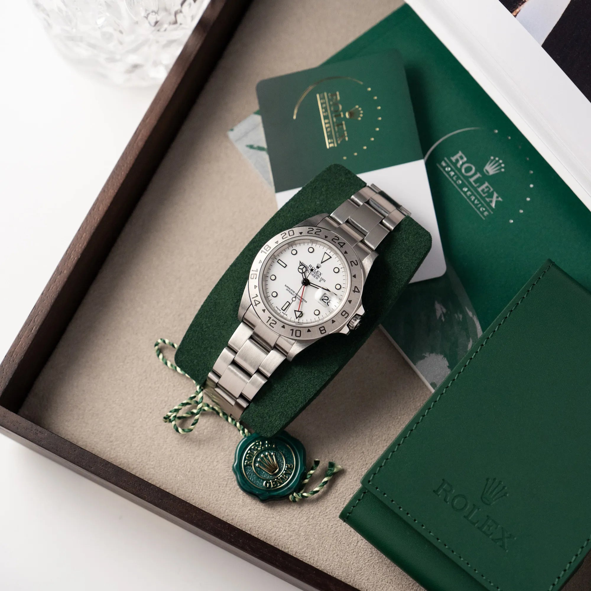 Produktfotografie der Rolex Explorer 2 - Referenz 16570T - mit dem weißen Polar-Zifferblatt zusammen mit der Servicekarte und dem Service-Etui