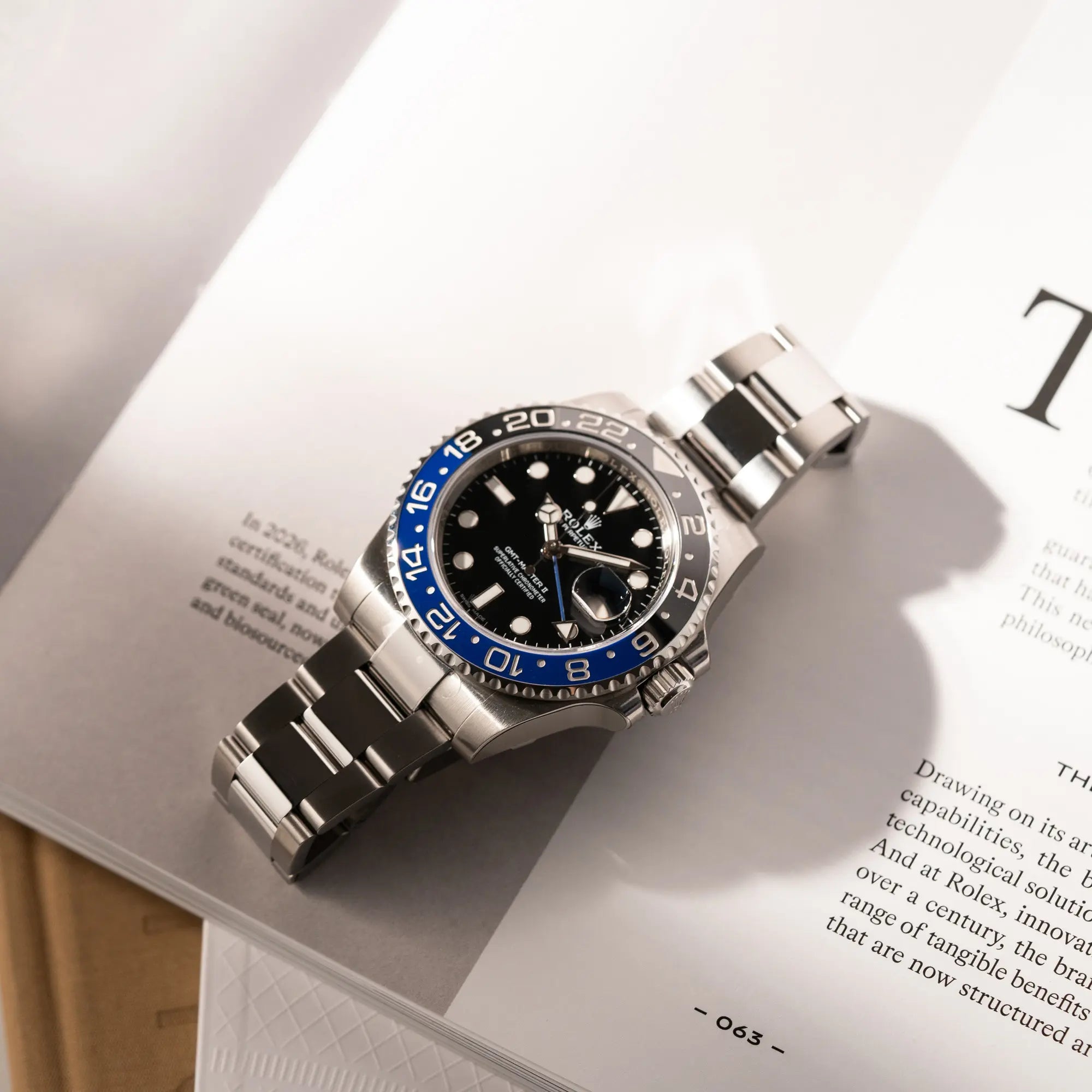 Rolex GMT-Master II der Referenz 116710BLNR mit dem Nickname "Batman" mit der schwarz blauen Keramik-Lünette am Oyster-Stahlband im verklebten Neuzustand liegt flach auf auf einem Buch über Rolex-Uhren