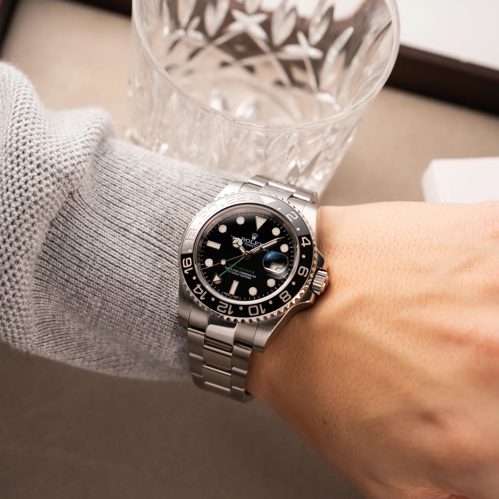 Mann in grauem Pullover trägt die Rolex GMT-Master II 116710LN mit schwarzer Keramik-Lünette und dem typischen grünem GMT-Zeiger an seinem Arm
