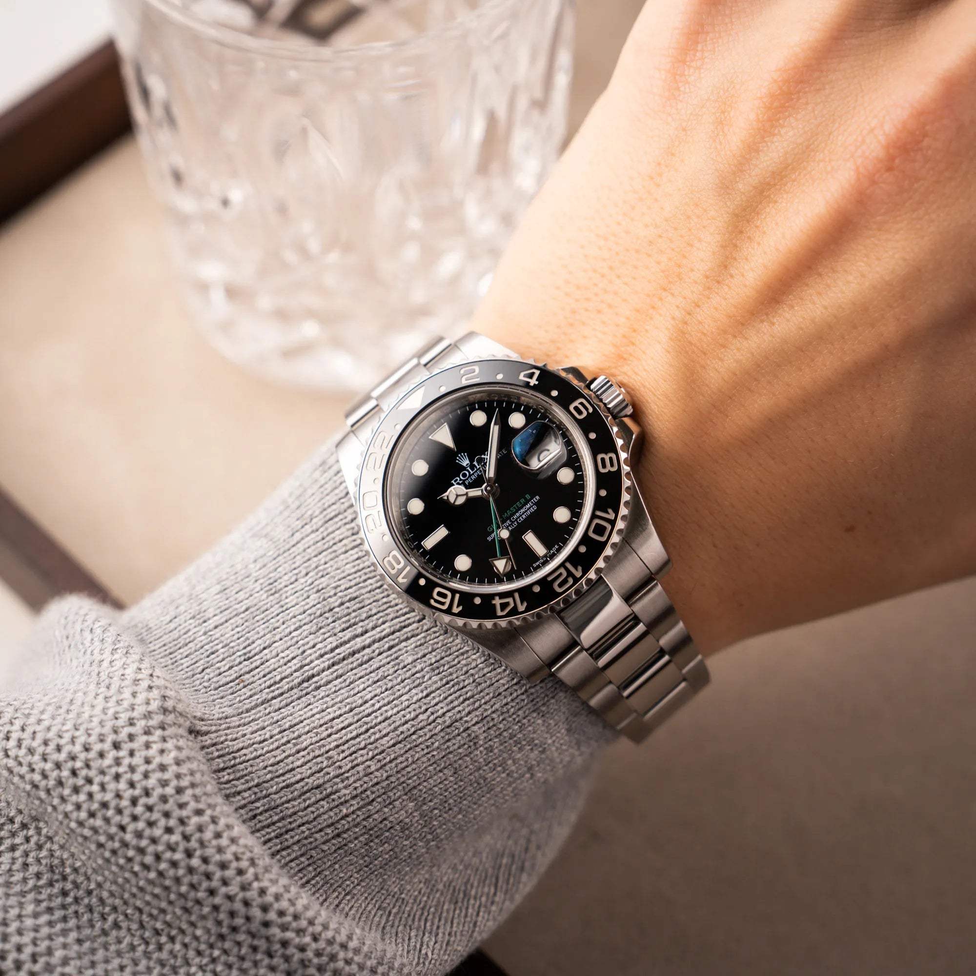 Mann in grauem Pullover trägt die Rolex GMT-Master II 116710LN mit schwarzer Keramik-Lünette und dem typischen grünem GMT-Zeiger an seinem Handgelenk und präsentiert die Uhr ind ie Kamera