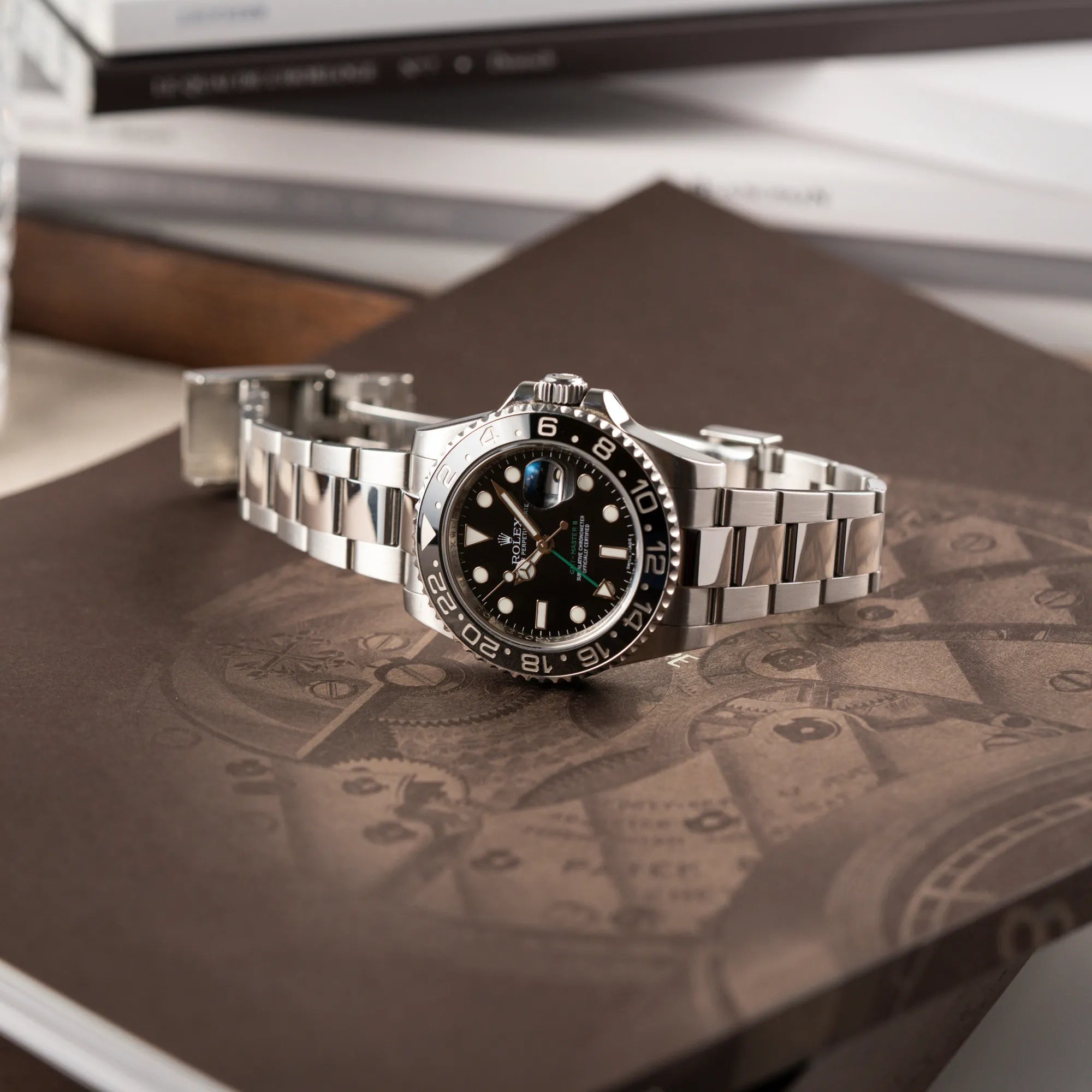 Rolex GMT-Master II 116710LN mit schwarzer Keramik-Lünette und dem typischen grünem GMT-Zeiger liegt auf braunem Uhrenbuch