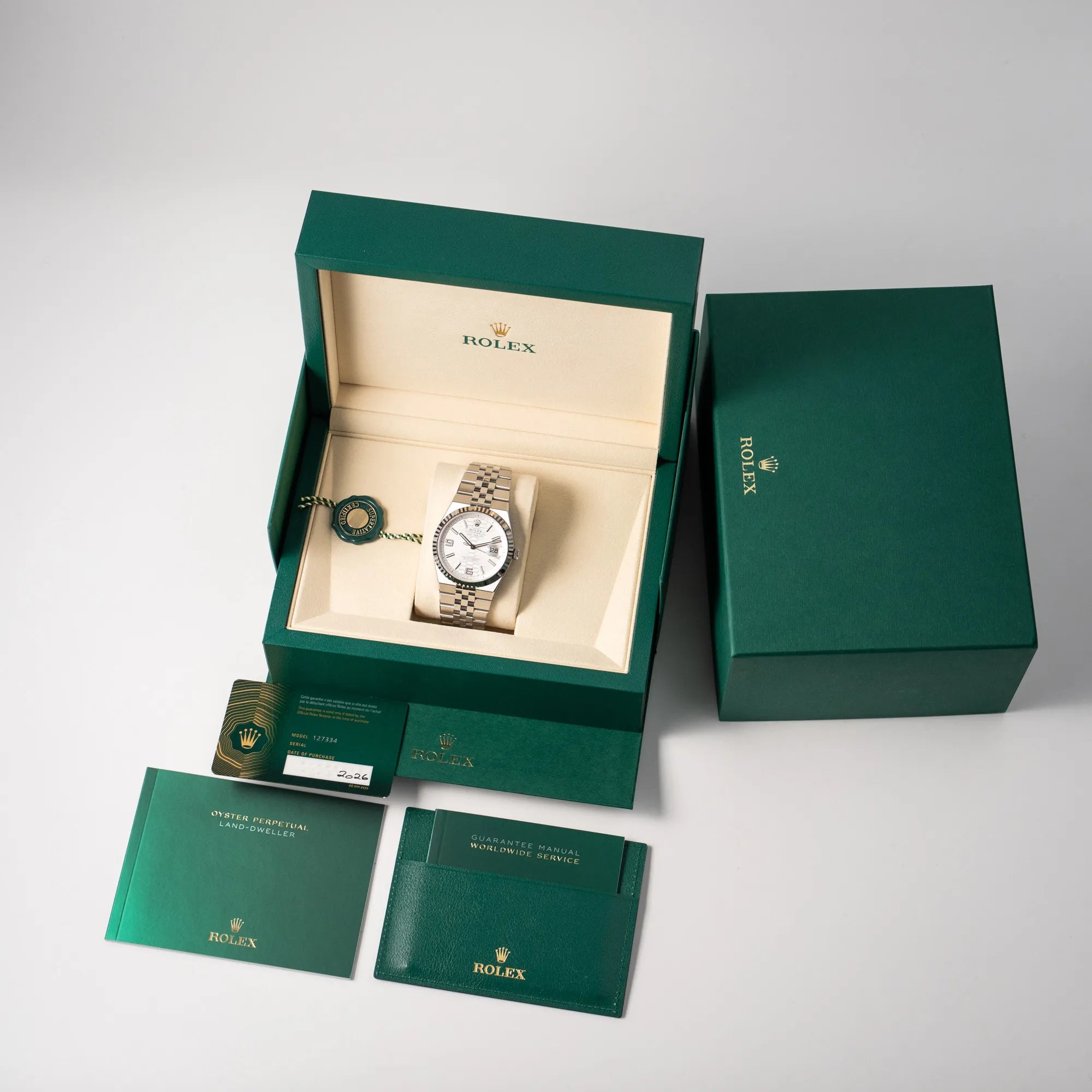 Lieferumfang zu der Rolex Land-Dweller 40 der Referenz 127334 im neuwertigen Zustand mit dem weißen Zifferblatt in Waben-Struktur am neuen Flat-Jubilee-Armband, bestehend aus Box mit Umkarton, Hangtag, allen Booklets und originaler Garantiekarte