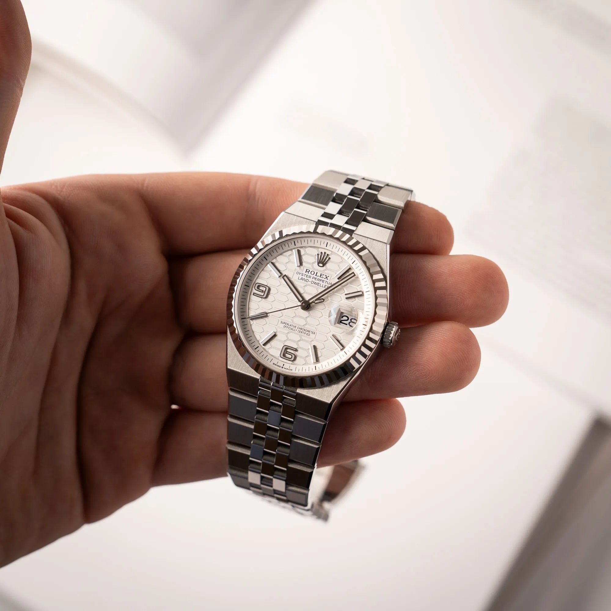 Mann hält die Rolex Land-Dweller 40 der Referenz 127334 im neuwertigen Zustand mit dem weißen Zifferblatt in Waben-Struktur am neuen Flat-Jubilee-Armband in seiner Hand und präsentiert die Uhr in die Kamera