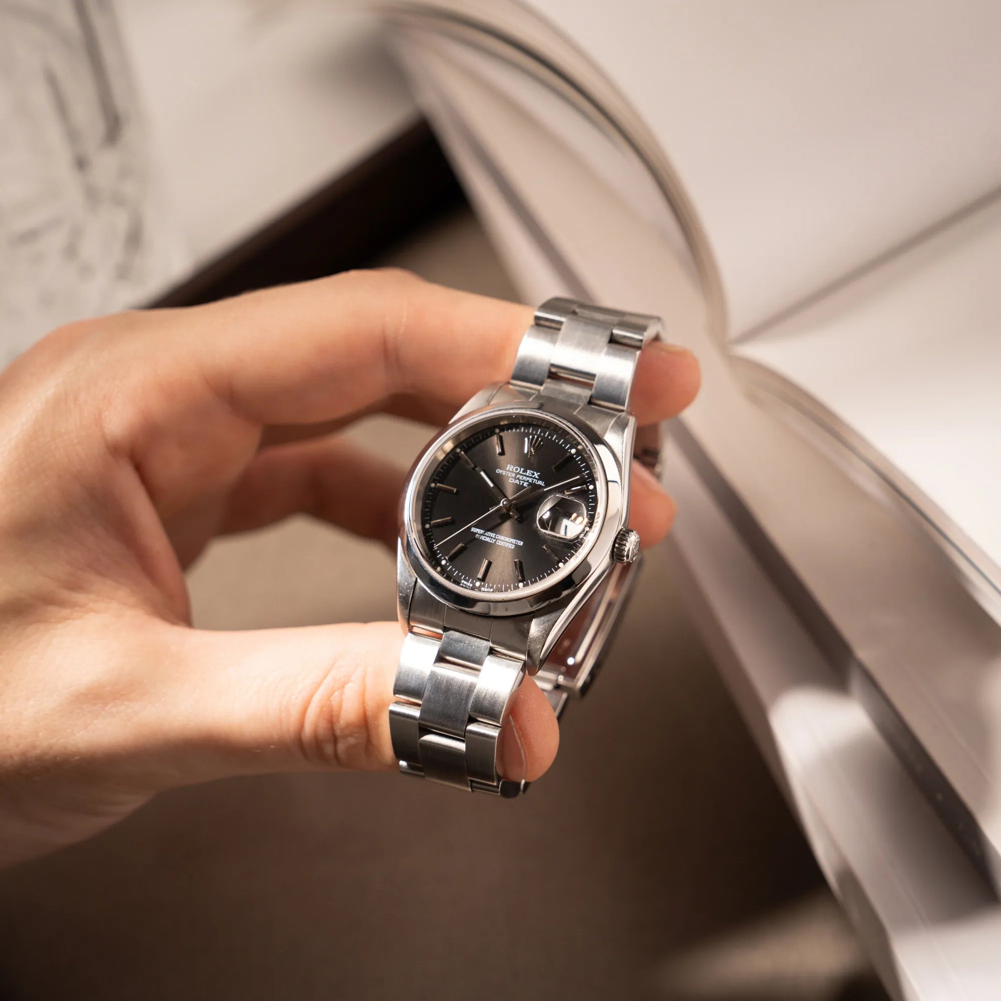 Mann hält die Rolex Oyster Perpetual 34 mit schwarzem Zifferblatt der Referenz 15200 mit glatter Lünette und 34mm Gehäusedurchmesser in seiner Hand und präsentiert die Uhr in die Kamera