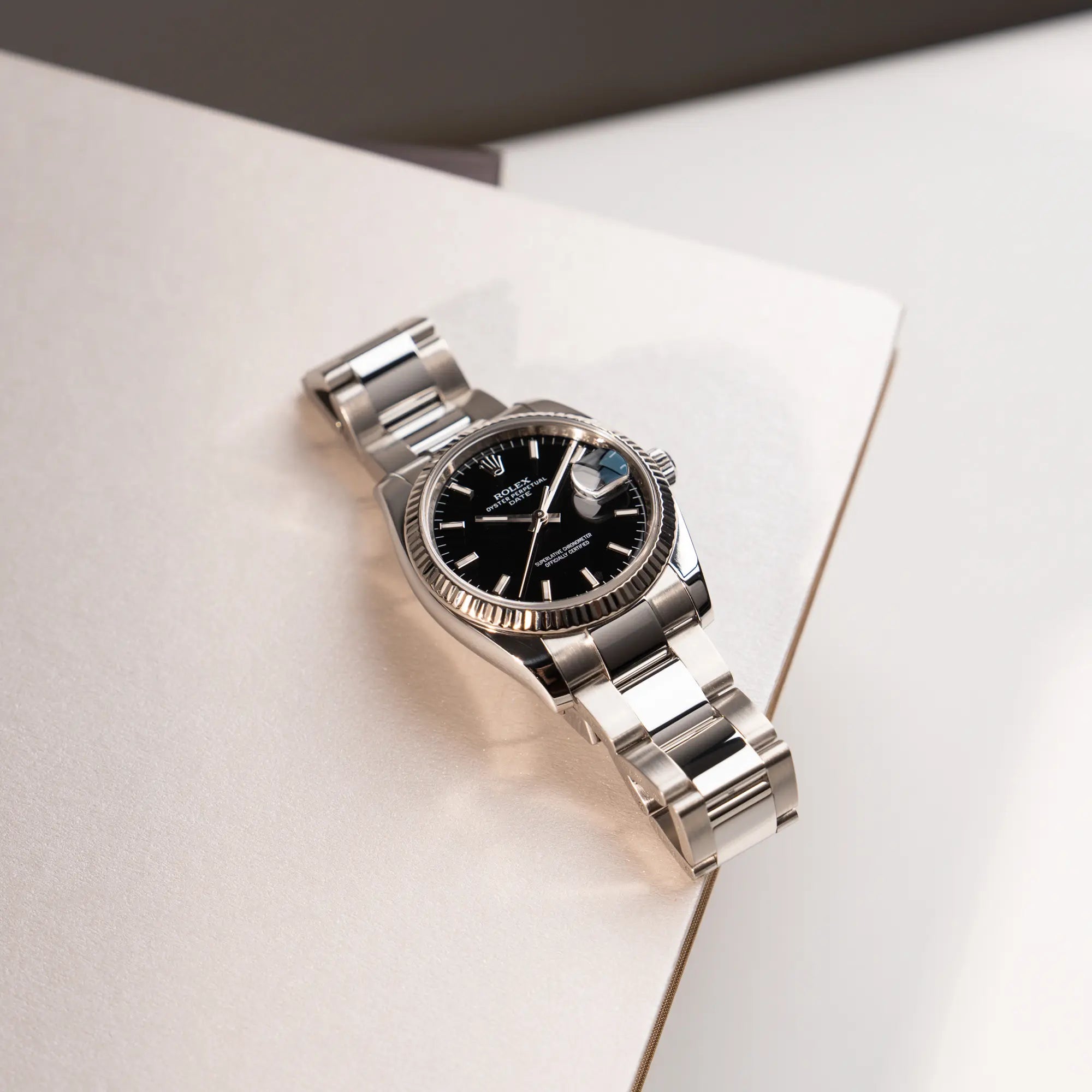 Produktfotografie der Rolex Oyster Perpetual Date 34 der Referenz 115234 mit schwarzem Zifferblatt und der geriffelten Weißgold-Lünette