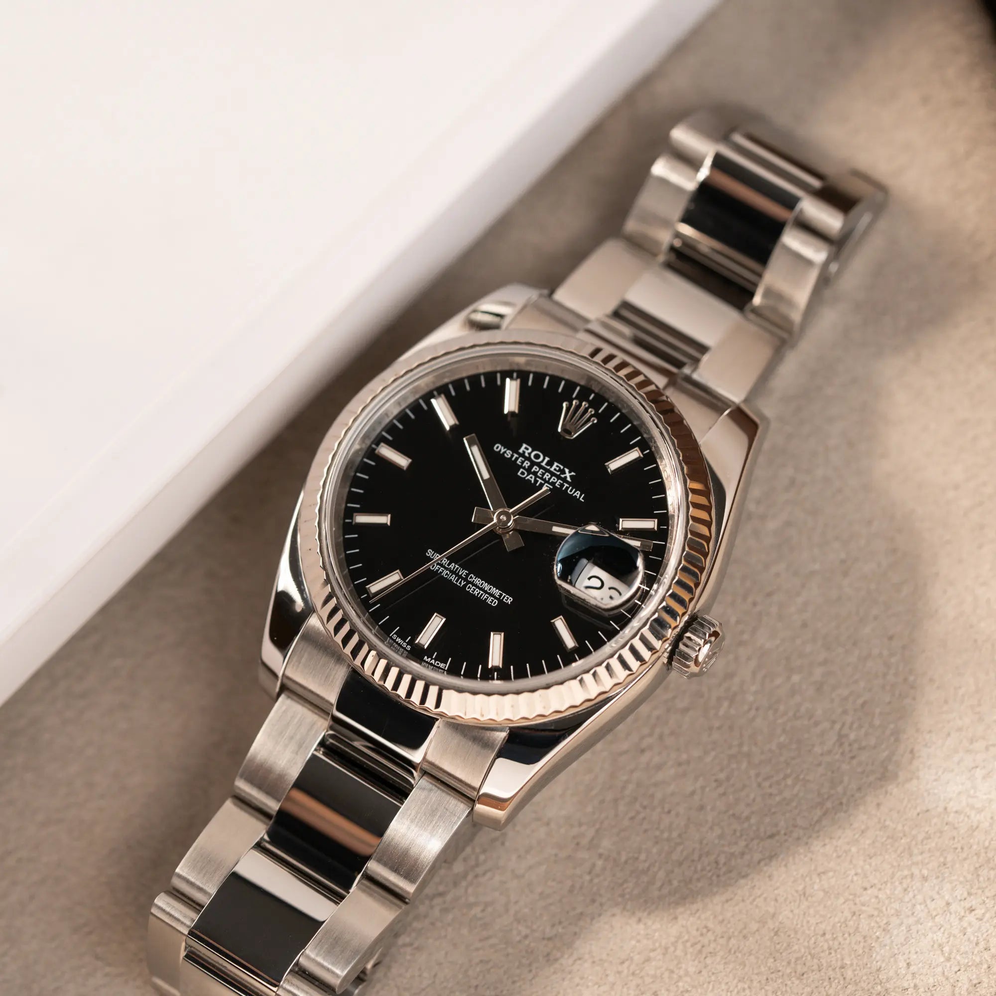 Rolex Oyster Perpetual Date 34 der Referenz 115234 mit schwarzem Zifferblatt und der geriffelten Weißgold-Lünette liegt auf einem Juwelierstablet
