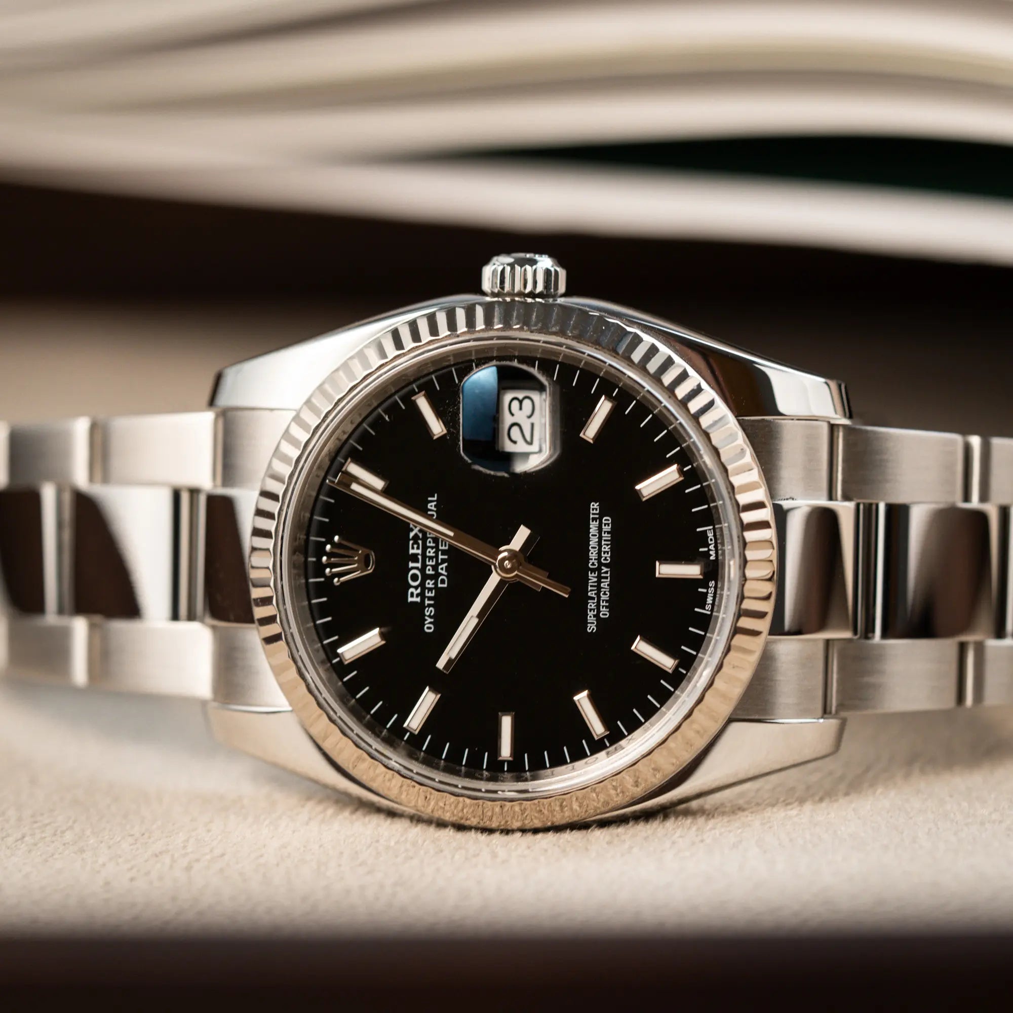 Detailaufnahme der seitlich auf dem Uhrengehäuse liegende Rolex Oyster Perpetual Date 34 der Referenz 115234 mit schwarzem Zifferblatt und der geriffelten Weißgold-Lünette