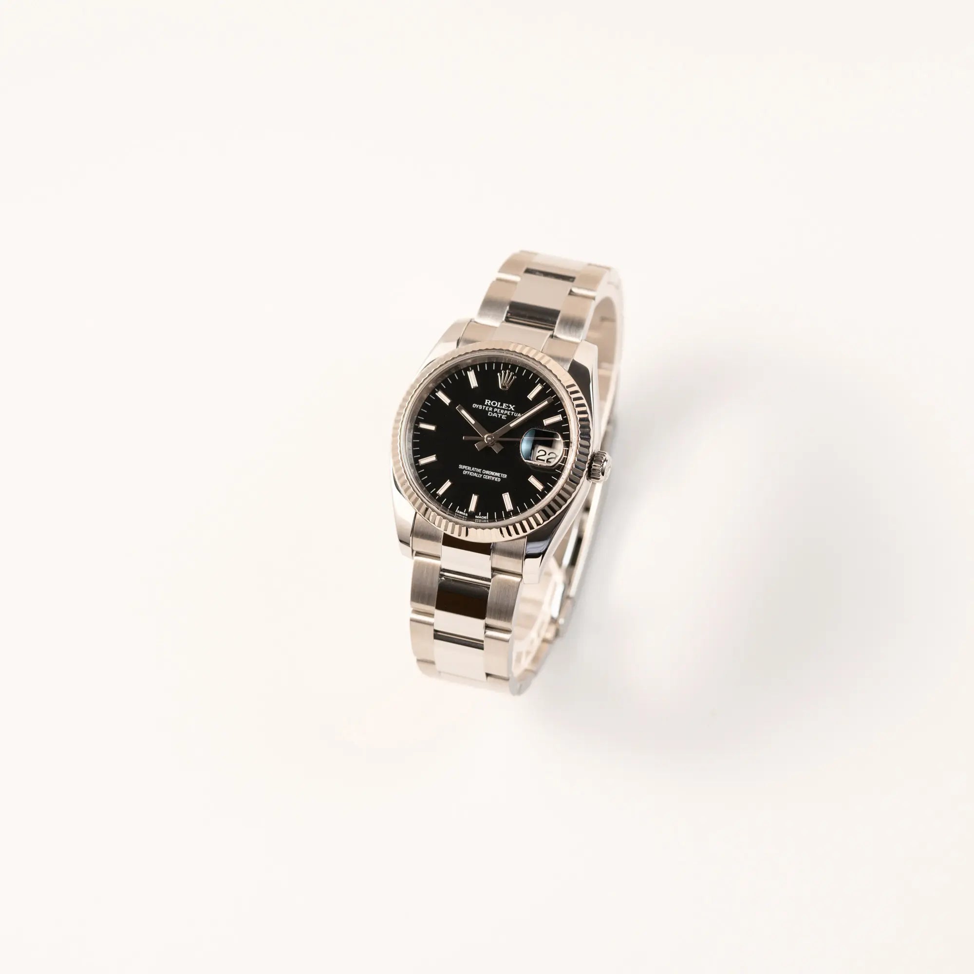 Leicht schräge Ansicht der Rolex Oyster Perpetual Date 34 der Referenz 115234 mit schwarzem Zifferblatt und der geriffelten Weißgold-Lünette