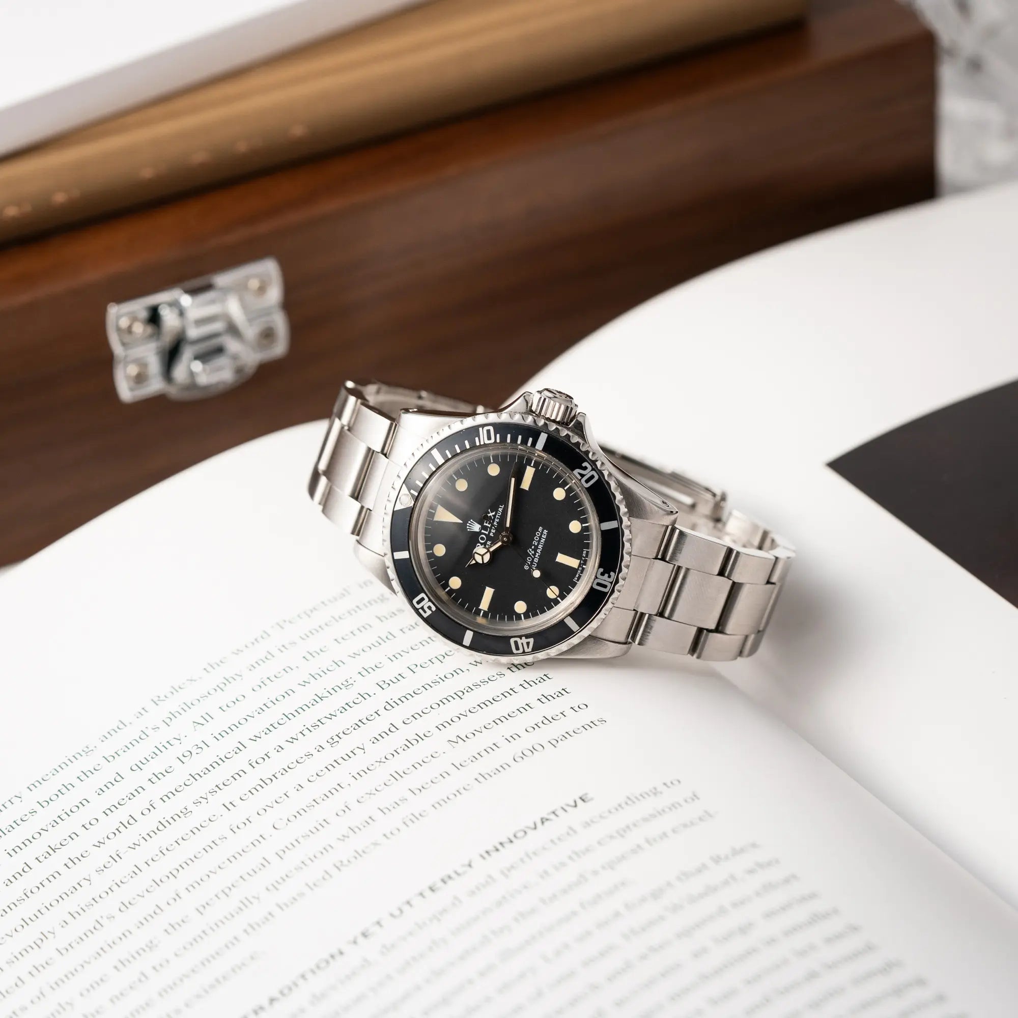 Produktfotografie zeigt die Rolex Submariner No Date MKII mit Serif Zifferblatt der Referenz 5513 aus 1970 mit gleichmäßiger Patina während die Uhr auf einem Rolex Magazin liegt