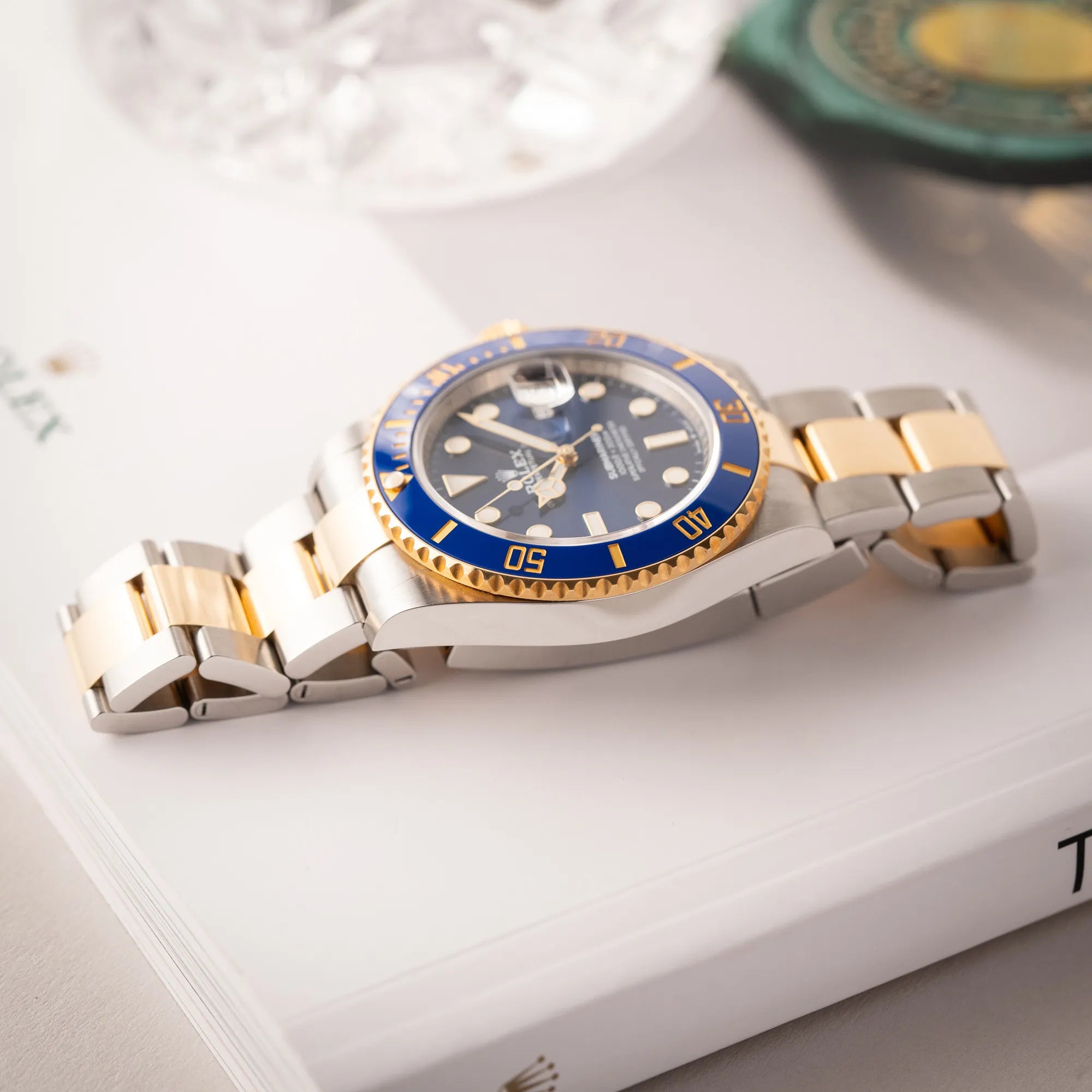 Rolex Submariner Date 126613LB Bluesy mit der typischen Kombination aus blauem Zifferblatt und Lünette mit dem Gehäuse und Armband aus Stahl-Gold liegt flach auf einem Buch über Rolex Uhren