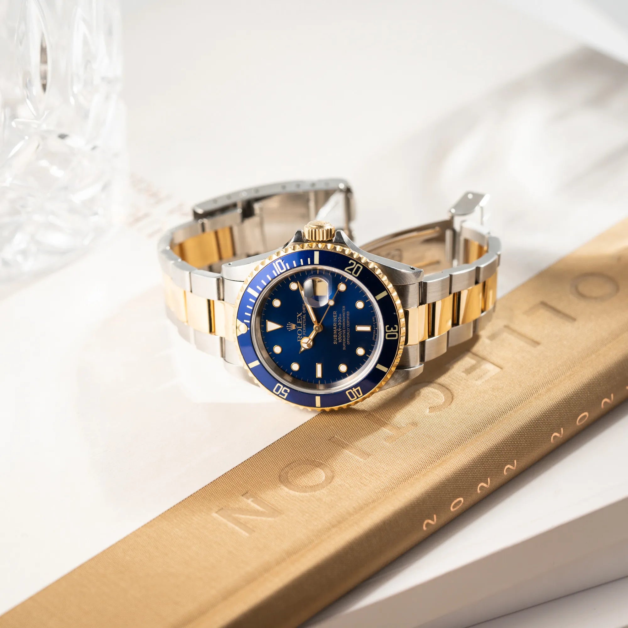 Produktfotografie der seitlich auf dem Uhrengehäuse liegenden bicolor Rolex Submariner Date der Referenz 16613 mit dem Spitznamen "Bluesy" in Stahl-Gold mit blauem Zifferblatt