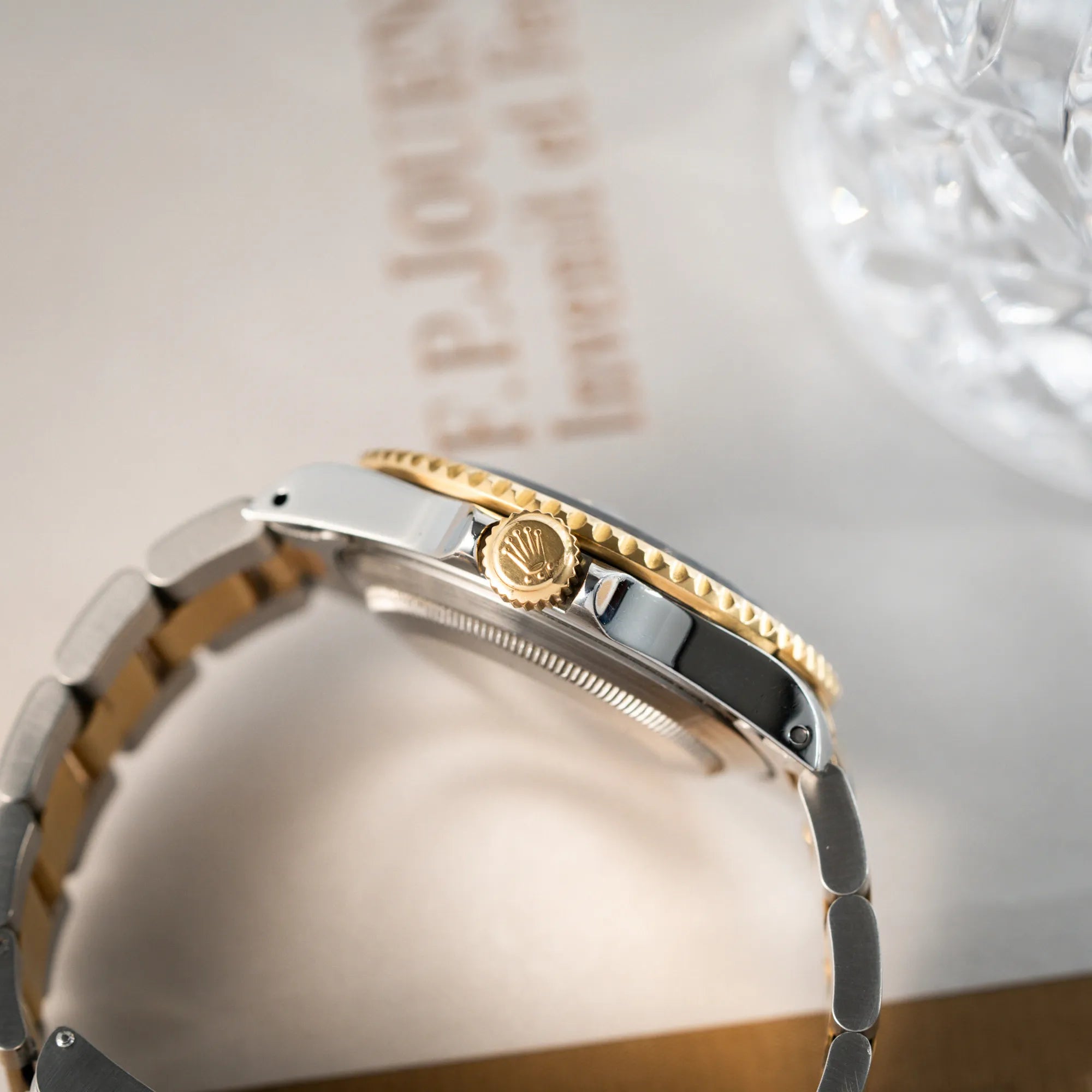 Produktfotografie der bicolor Rolex Submariner Date der Referenz 16613 mit dem Spitznamen "Bluesy" in Stahl-Gold mit blauem Zifferblatt zeigt die seitliche Flanke des Uhrengehäuses mit Blick auf die goldene Aufzugskrone und den goldenen Lünettenring