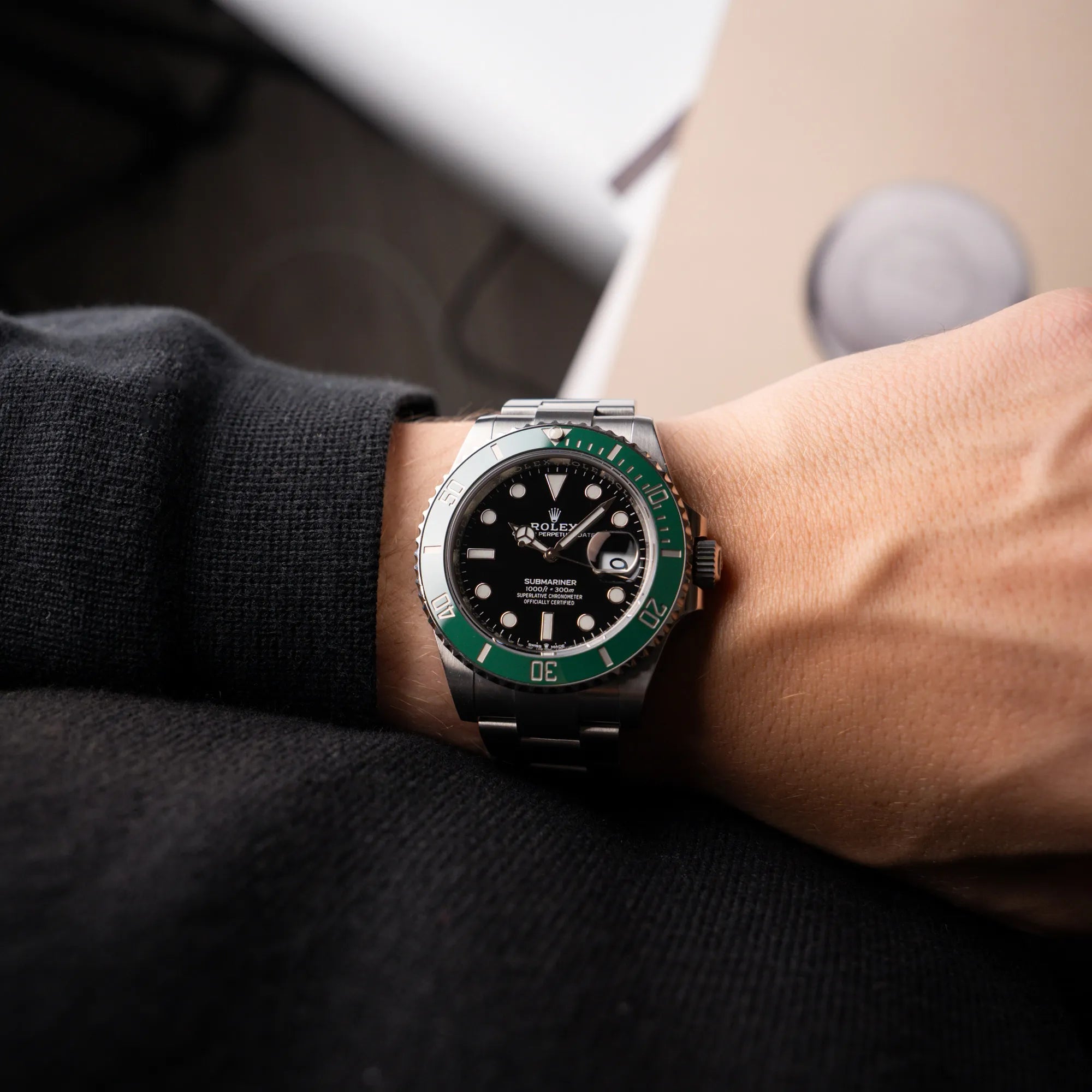 Mann trägt die Rolex Submariner Date Starbucks 126610LV mit schwarzem Zifferblatt und grüner Cerachrom-Lünette am Arm, während sich das Licht auf der glänzenden Lünette bricht