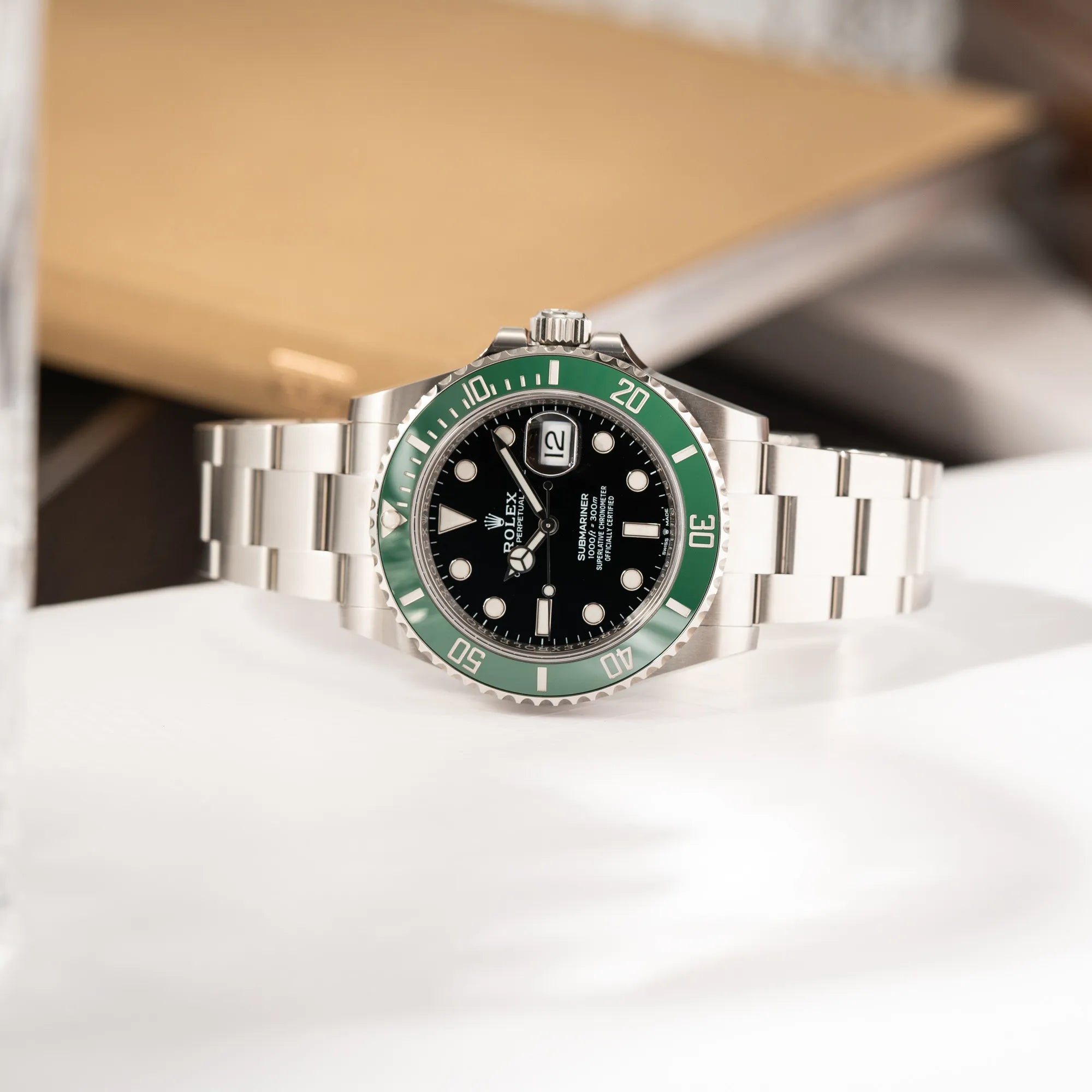 Produktfotografie der seitlich auf dem Uhrengehäuse liegenden Rolex Submariner Date "Starbucks" der Referenz 126610LV mit der modelltypischen grünen Keramik-Lünette, die im Kontrast zu dem schwarzen Zifferblatt steht