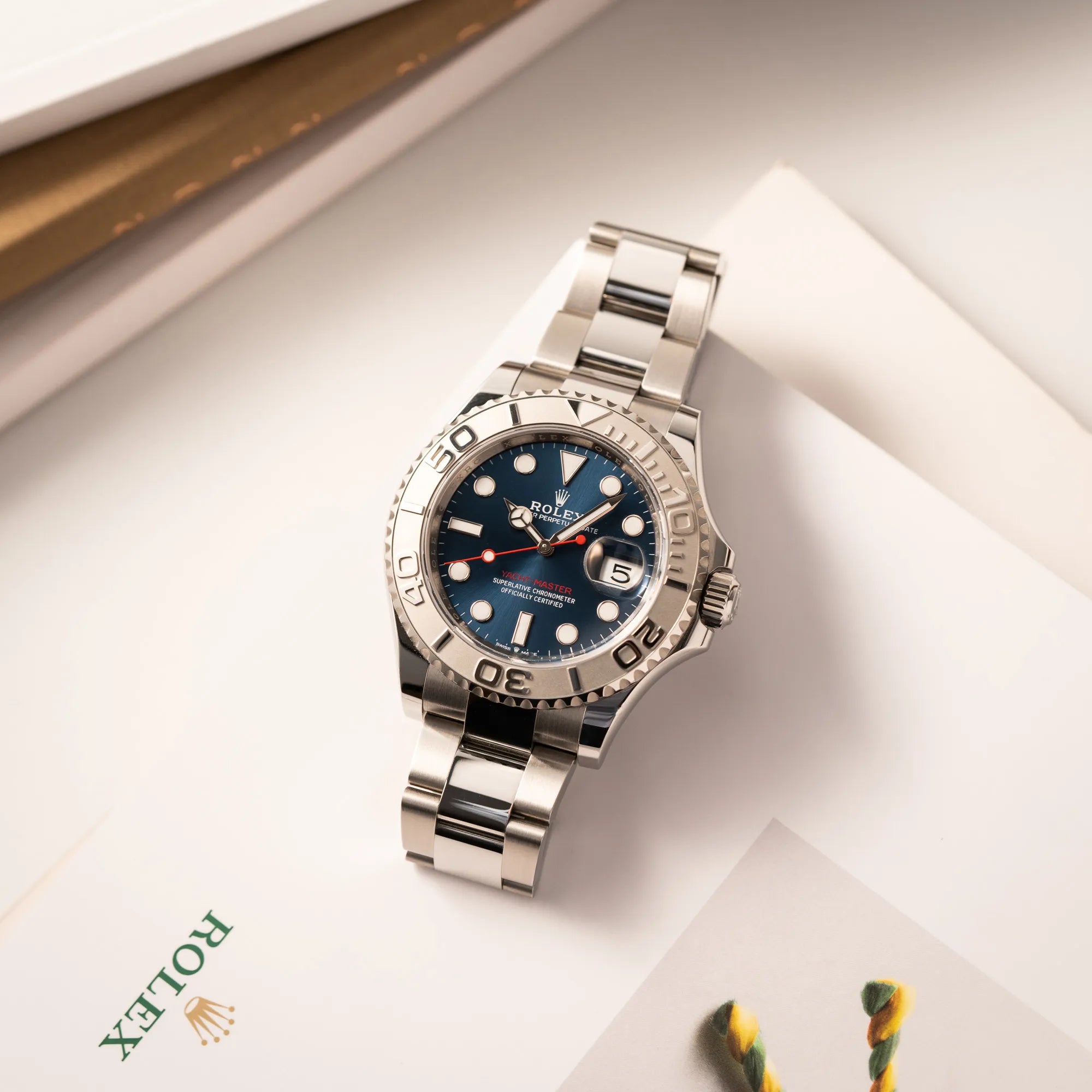 Produktfotografie der flach auf einem Rolex Buch liegenden Rolex Yacht-Master 40 der Referenz 126622 mit der Platin-Lünette in der blauen Zifferblatt-Variante