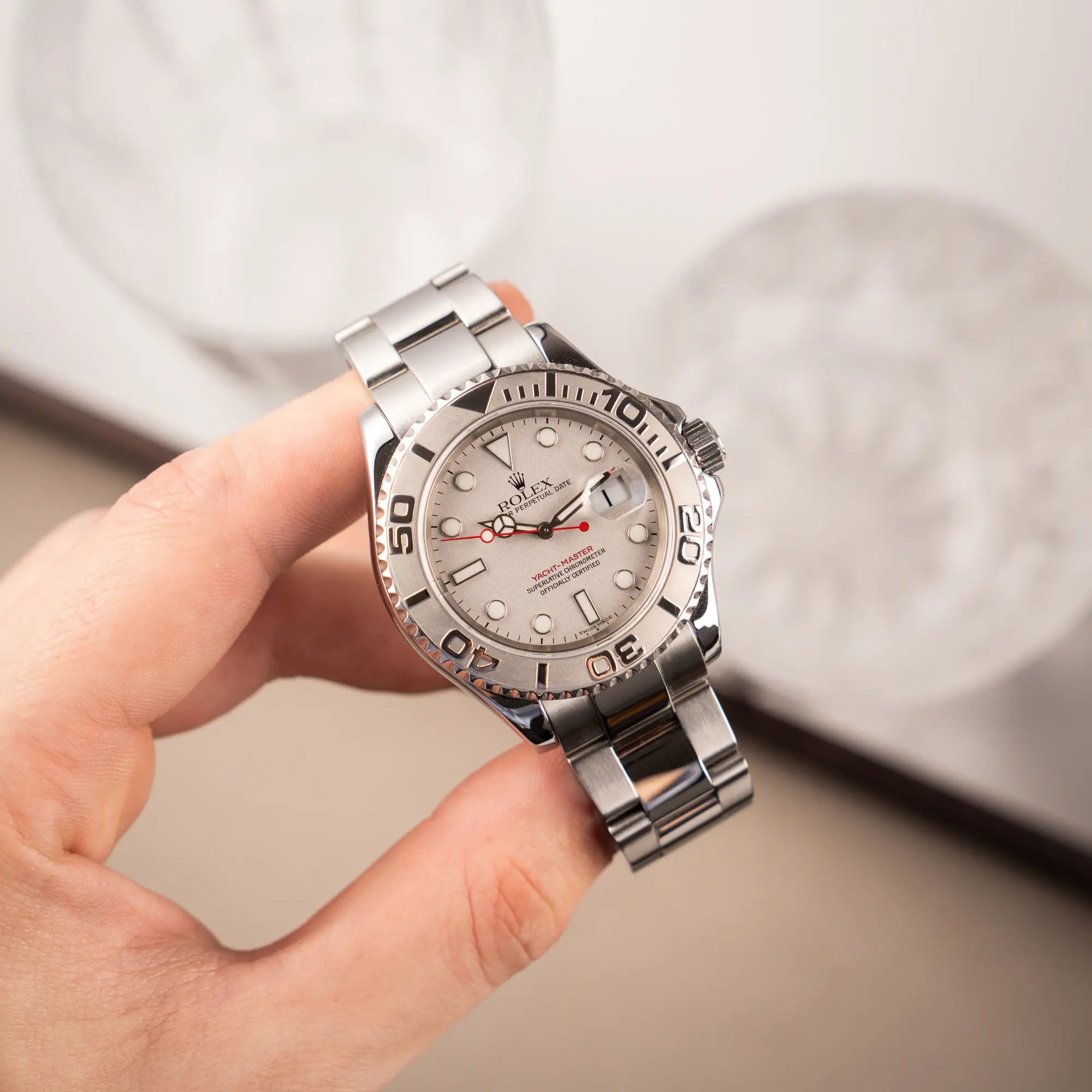 Mann hält die Rolex Yachtmaster 40 Platinum mit der Referenz 16622 mit Platin-Lünette und dem typischen roten Sekundenzeiger in seiner Hand und präsentiert die Uhr in die Kamera