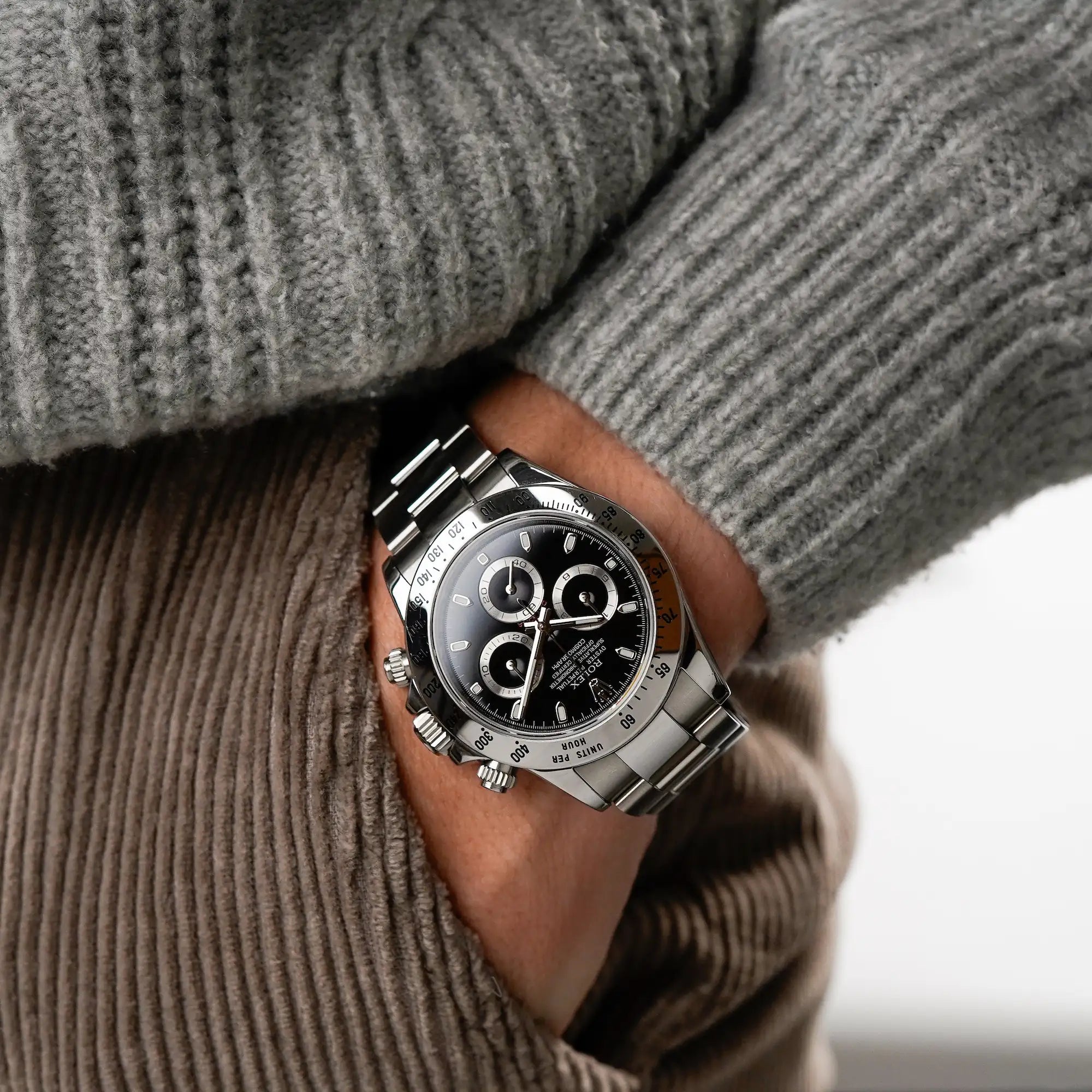 Mann trägt die Rolex Cosmograph Daytona 116520 mit dem schwarzen Zifferblatt und der Edelstahl-Lünette an seinem Handgelenk, während seine Hand in der Tasche seiner Kord-Hose steckt