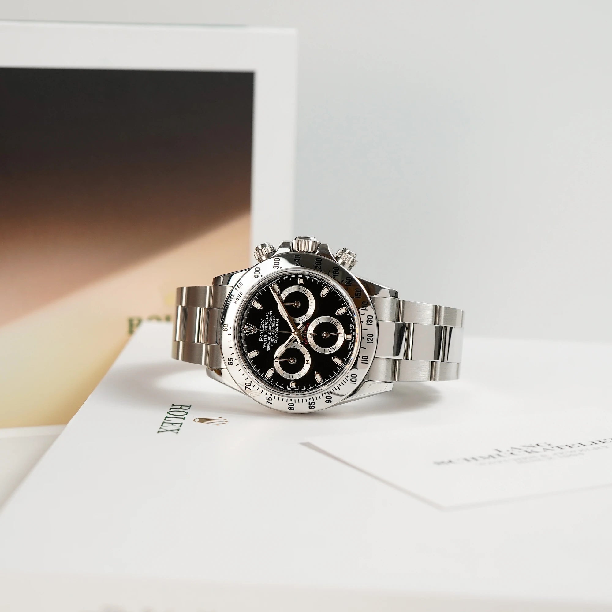 Rolex Cosmograph Daytona mit dem schwarzen Zifferblatt und der Edelstahl-Lünette liegt seitlich auf einem Heft von Rolex