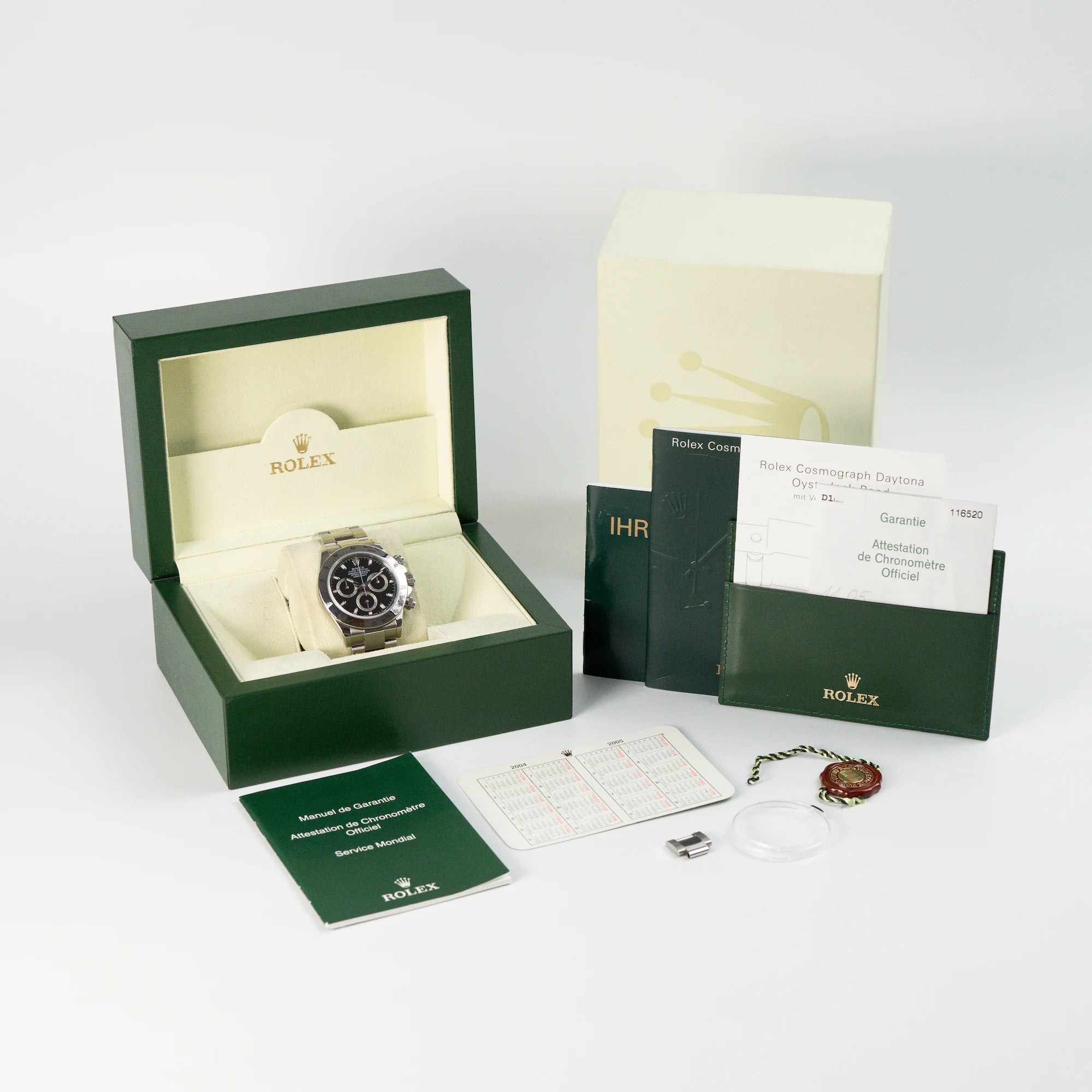 Lieferumfang der Rolex Cosmograph Daytona, Referenz 116520, mit schwarzem Zifferblatt, bestehend aus Box, Booklets, Garantiekarte, Hang-Tags und Lünettenschutz