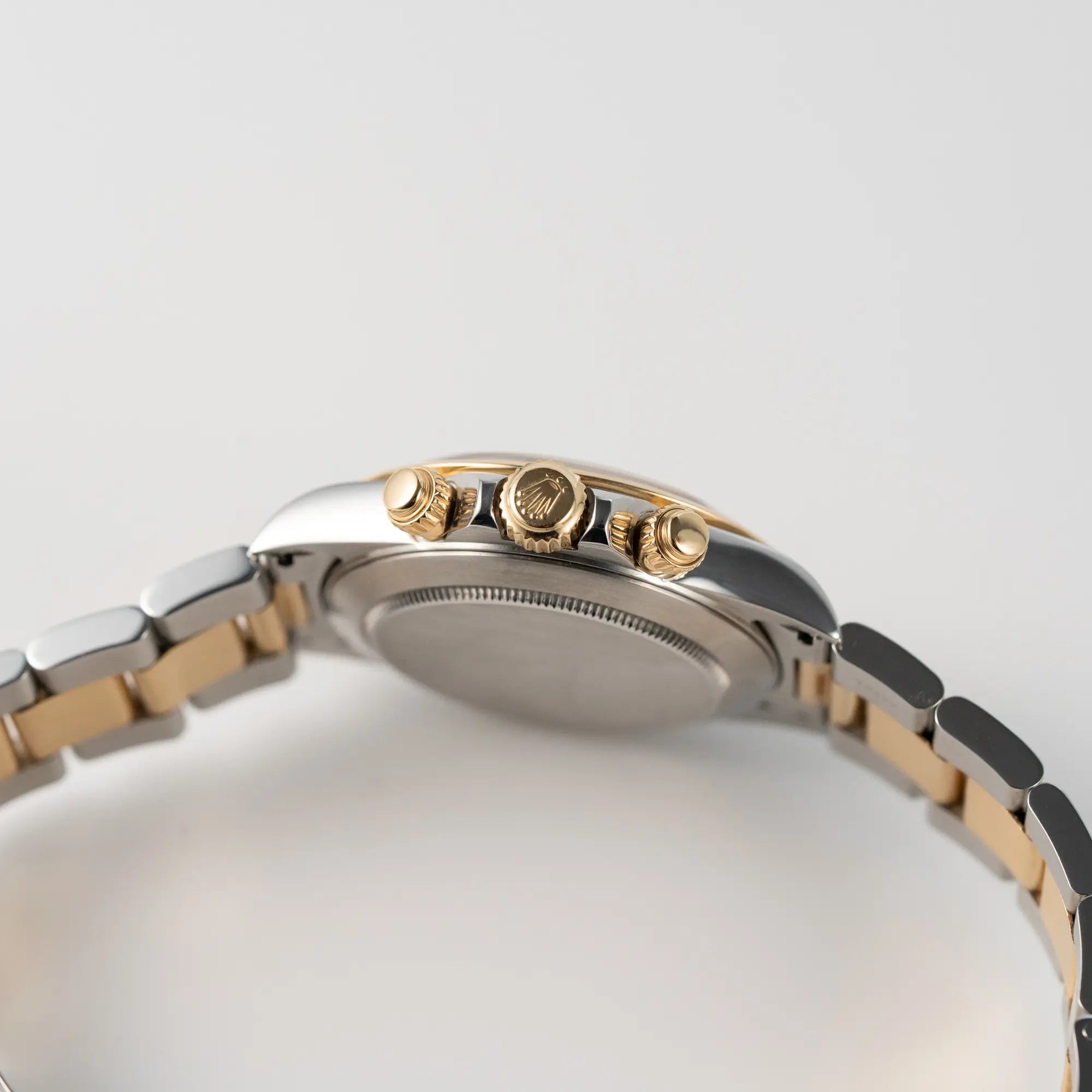 Seitliches Uhrengehäuse der Rolex Zenith Daytona in Stahl-Gold mit goldfarbenem Zifferblatt mit Blick auf die goldene Aufzugskroneund Chronographen-Drücker