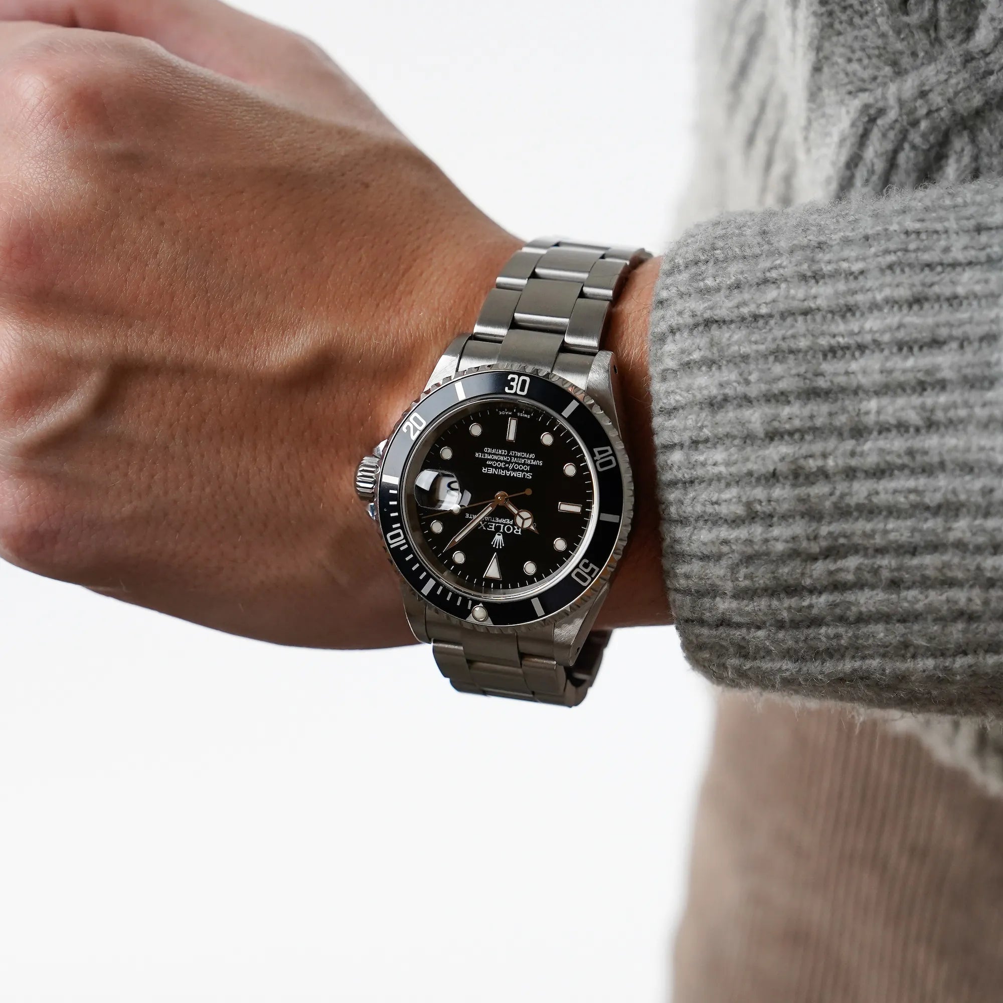 Mann trägt die Rolex Submariner Date in schwarz, Referenz 16610, mit Flat-Four-Lünette am Handgelenk und präsentiert diese in die Kamera