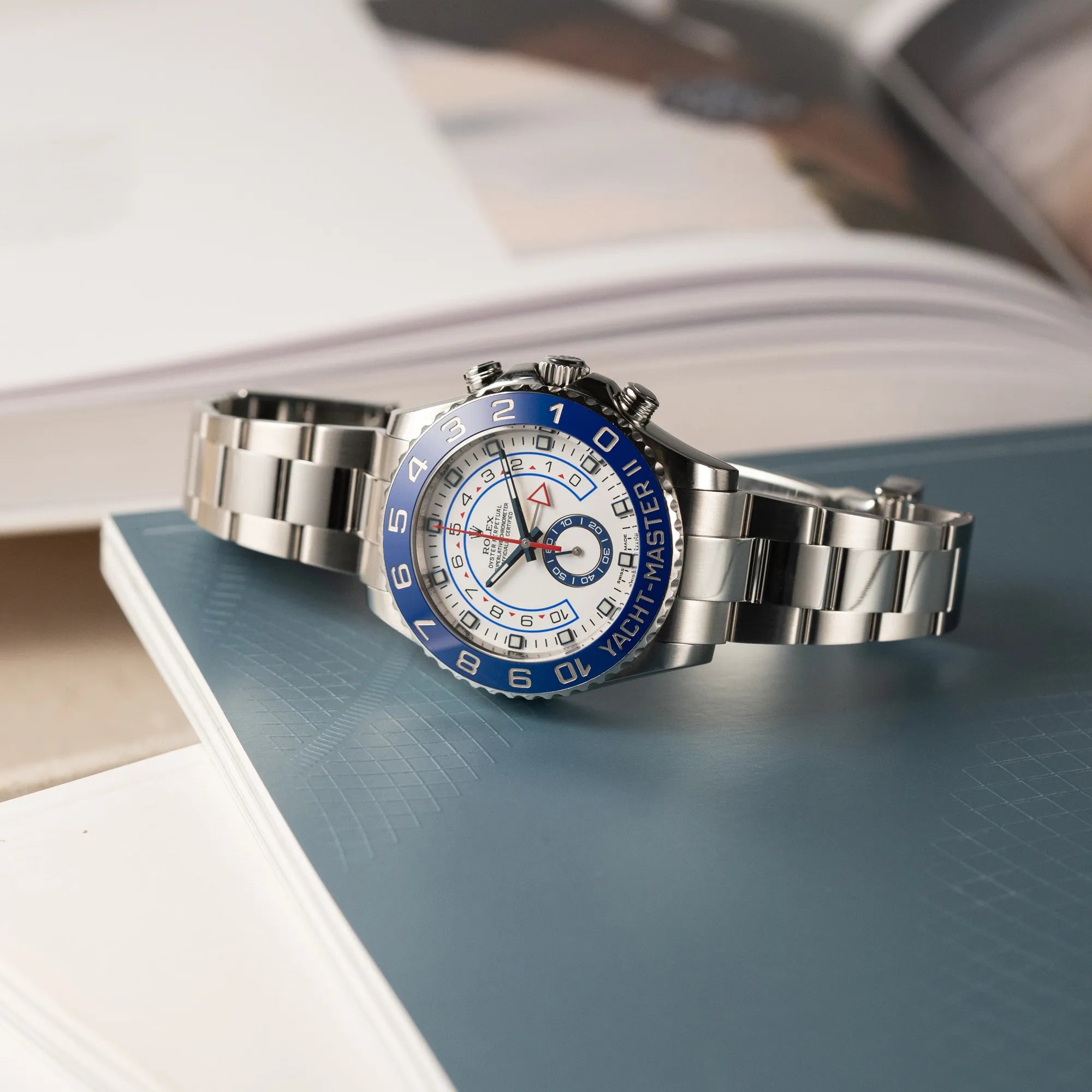 Produktfotografie der Rolex Yacht-Master 2 mit weißem Zifferblatt und blauer Lynette auf einem petrolfarbenem Buch