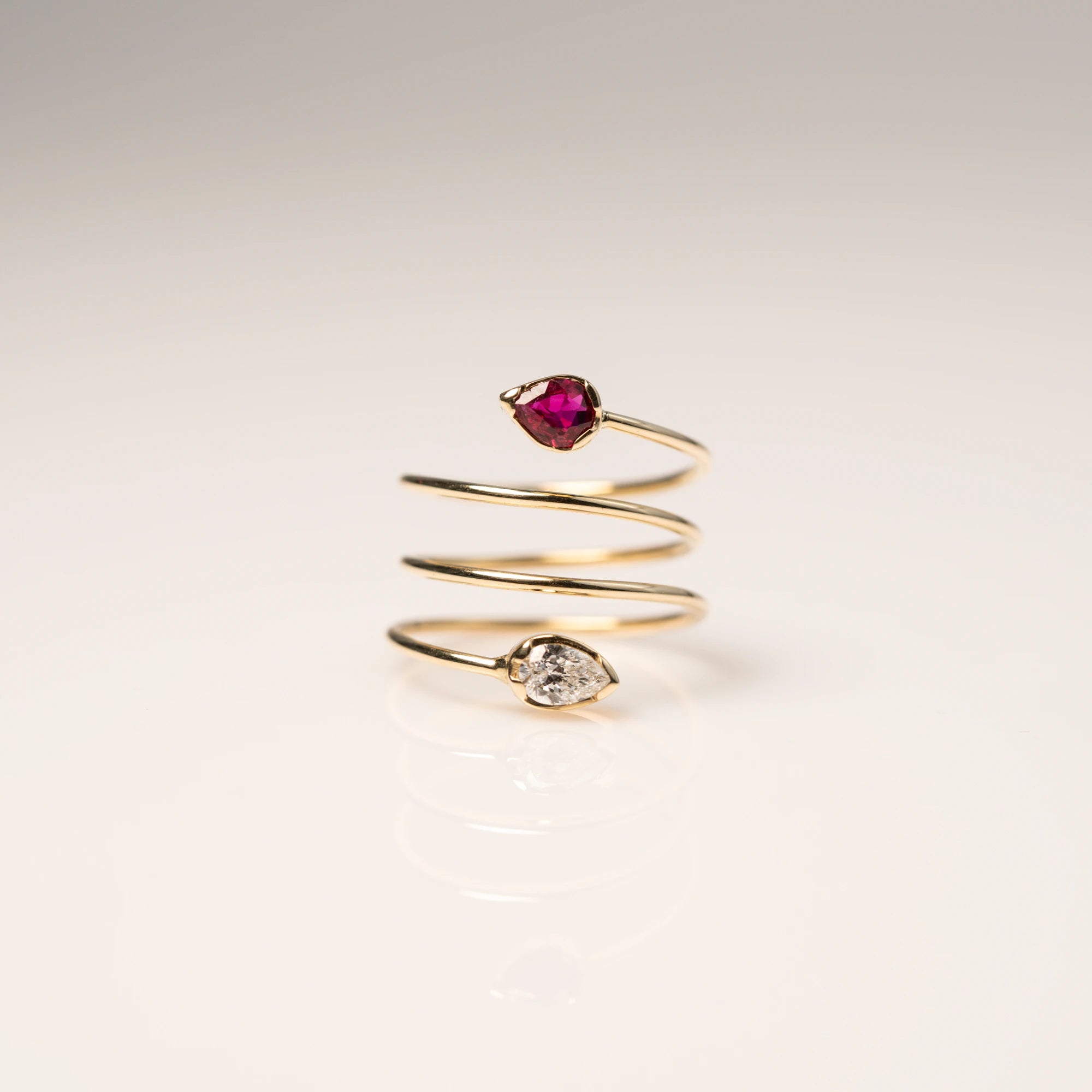 Produktfotografie des Gelbgoldrings "Twisted Drop" aus der Schmuckatelier Lang Collection, der an eine Spirale erinnert und als Blickfang zum Abschluss der offenen Ringschiene einen Rubin und einen funkelnden Brillanten in Tropfenform verbaut hat