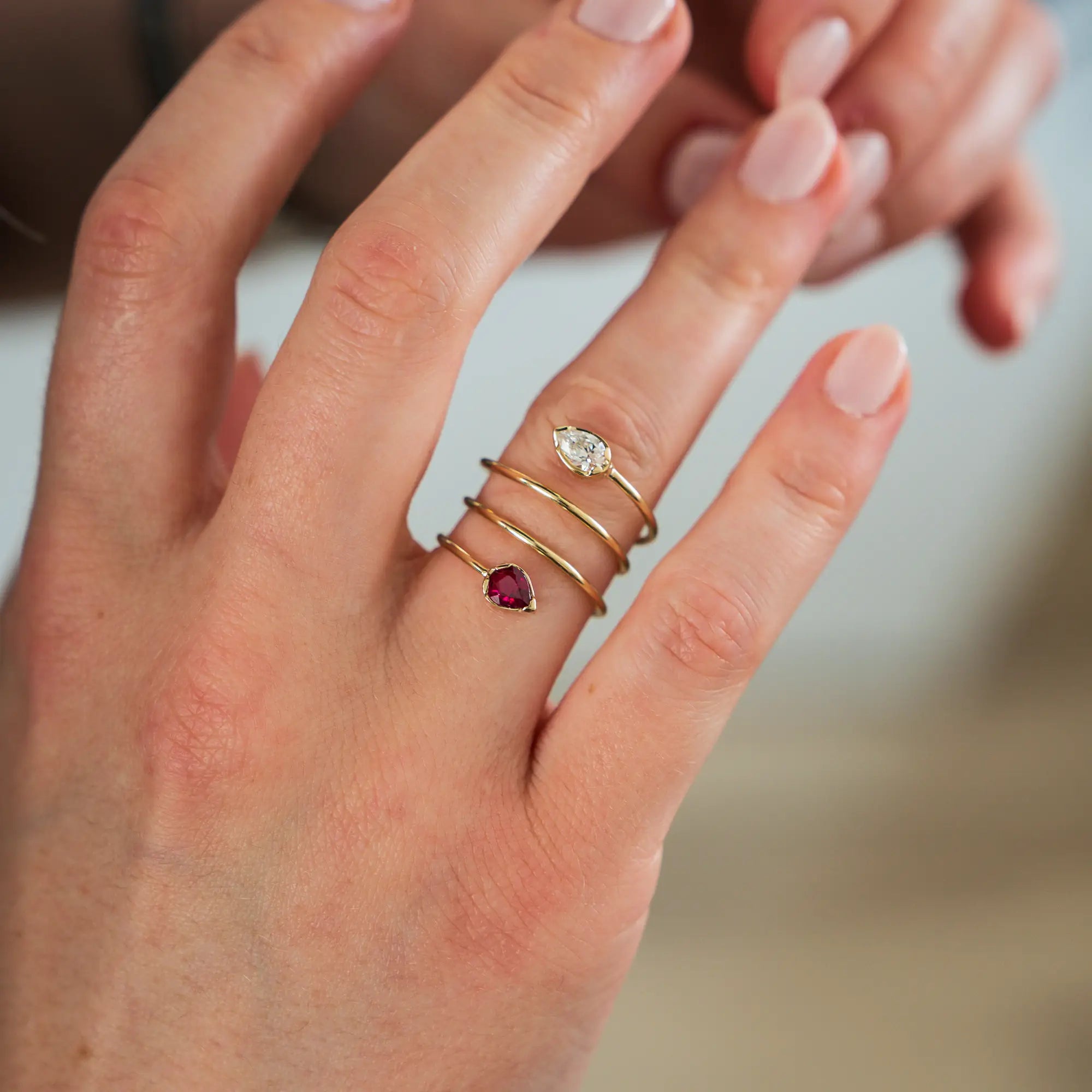 Frau trägt den Gelbgoldring "Twisted Drop" aus der Schmuckatelier Lang Collection an ihrem RIngfinger, der an eine Spirale erinnert und als Blickfang zum Abschluss der offenen Ringschiene einen Rubin und einen funkelnden Brillanten in Tropfenform verbaut hat