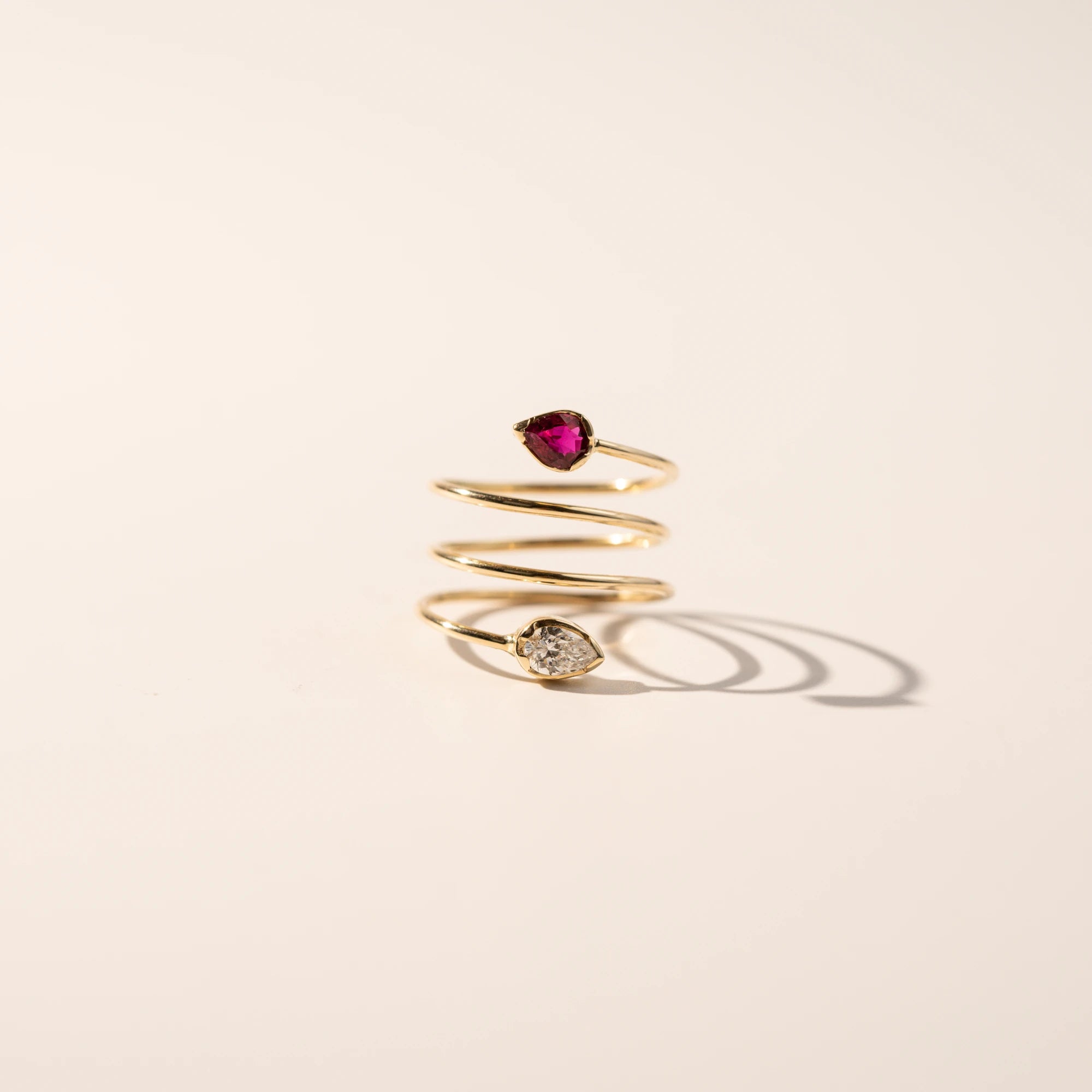 Produktfotografie des Gelbgoldrings "Twisted Drop" aus der Schmuckatelier Lang Collection, der an eine Spirale erinnert und als Blickfang zum Abschluss der offenen Ringschiene einen Rubin und einen funkelnden Brillanten in Tropfenform verbaut hat, während die Lichtstrahlen im Gold funkeln